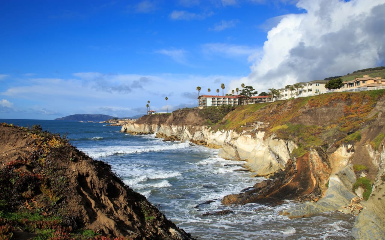 Serene clifftop houses overlooking a vast expanse of ocean, vibrant sky, and gentle waves.