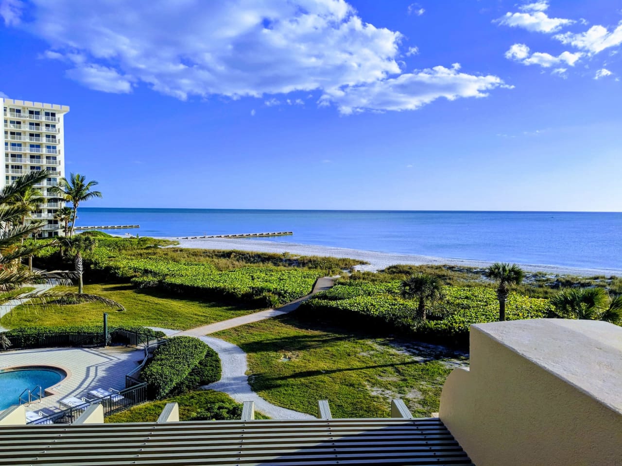 Turquoise waters lap at pristine white sand, framed by swaying palm trees and and a resort complex in the distance.