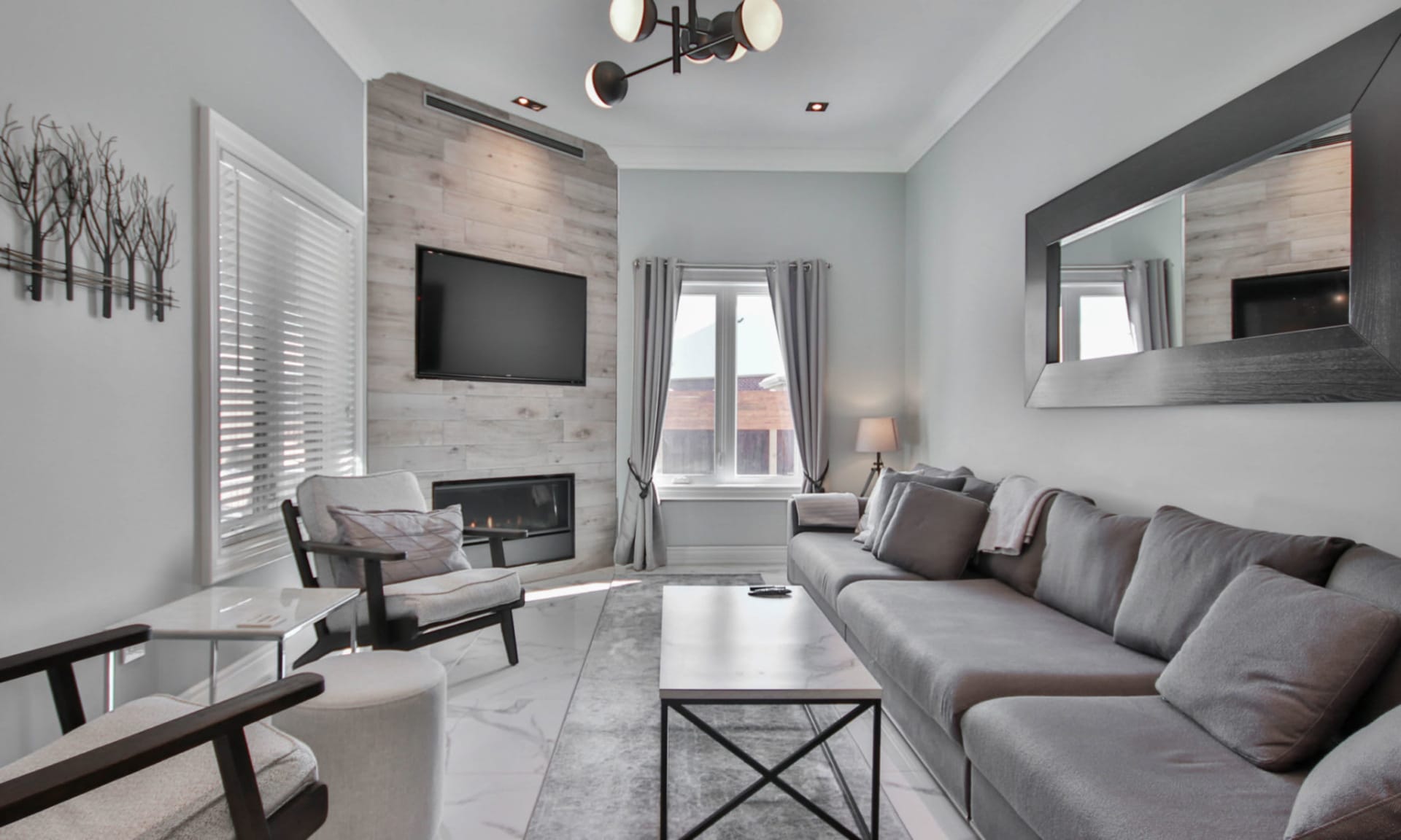 Modern living room with a gray sectional, wall-mounted television, and linear fireplace.