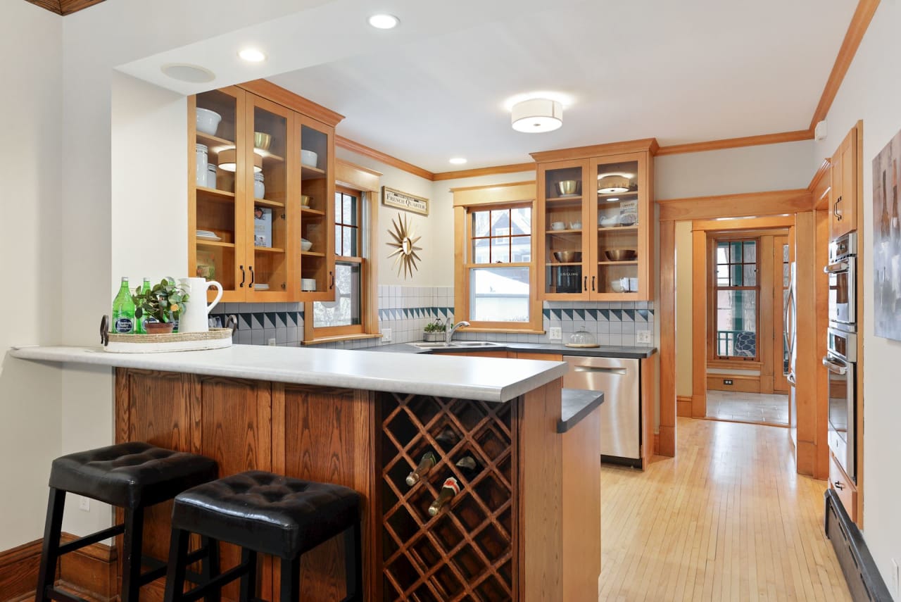 A kitchen with wooden cabinets and a wine rack attached to a wooden bar with stools.