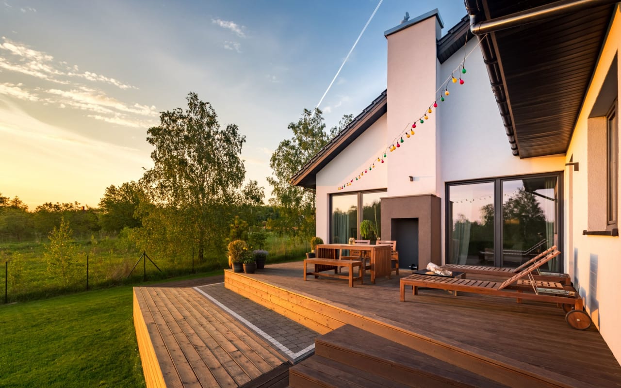 A wooden deck with a table and chairs beside a lush landscape.