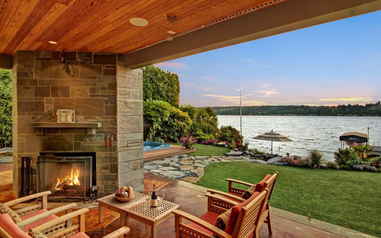 A patio with a fireplace and chairs overlooking a lake