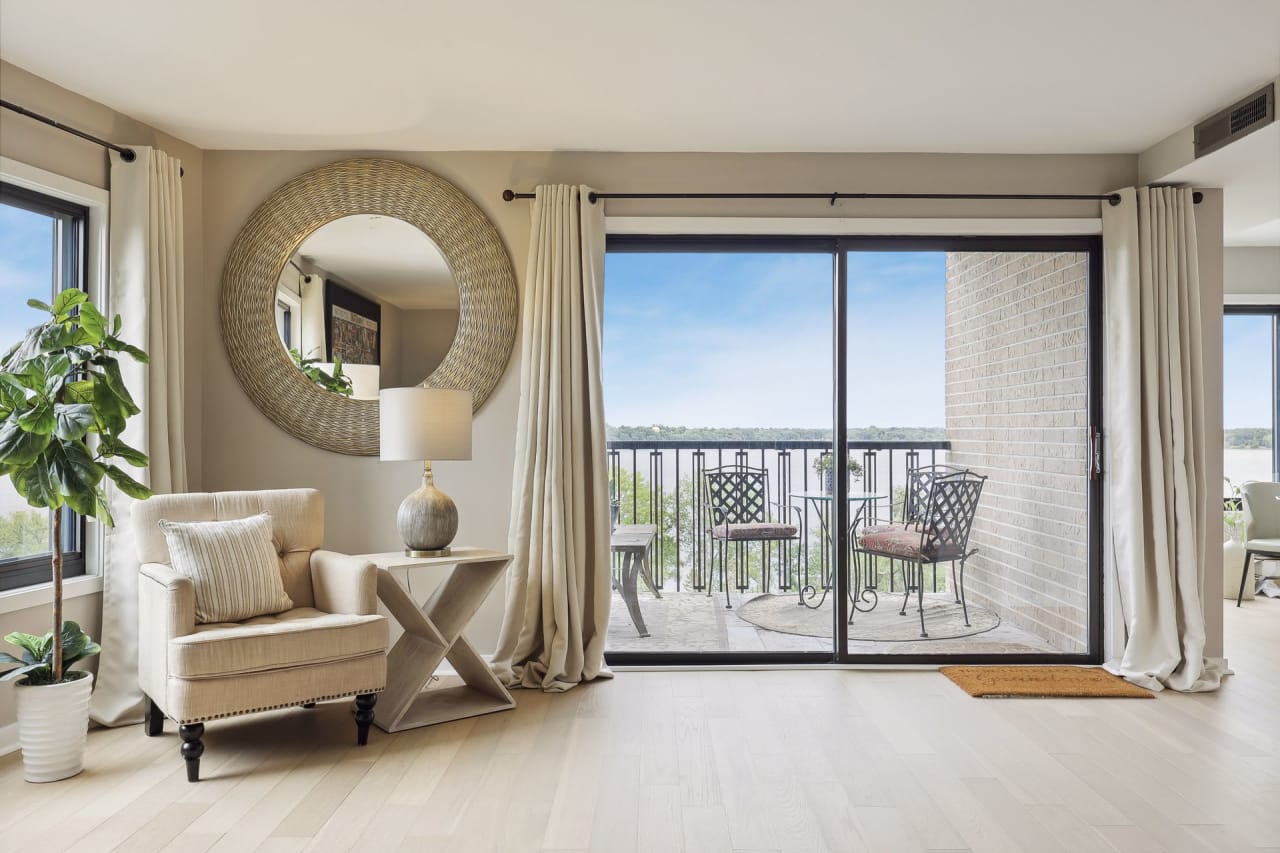 A room with a chair, a wooden coffee table, and a large mirror mounted on the wall beside the balcony.