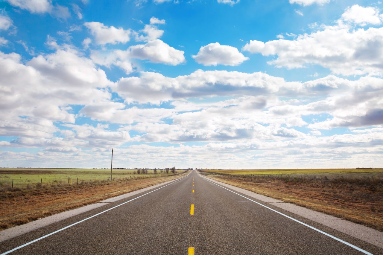 An empty highway with a blue sky and white clouds.