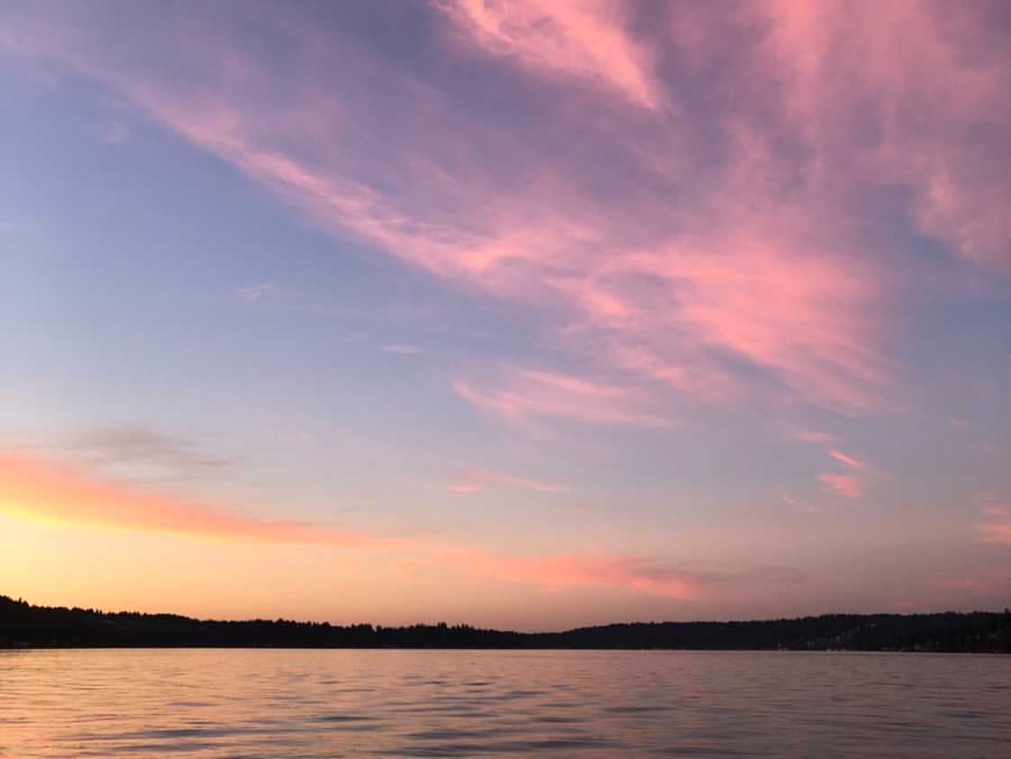 A sunset over a lake with pink clouds in the sky