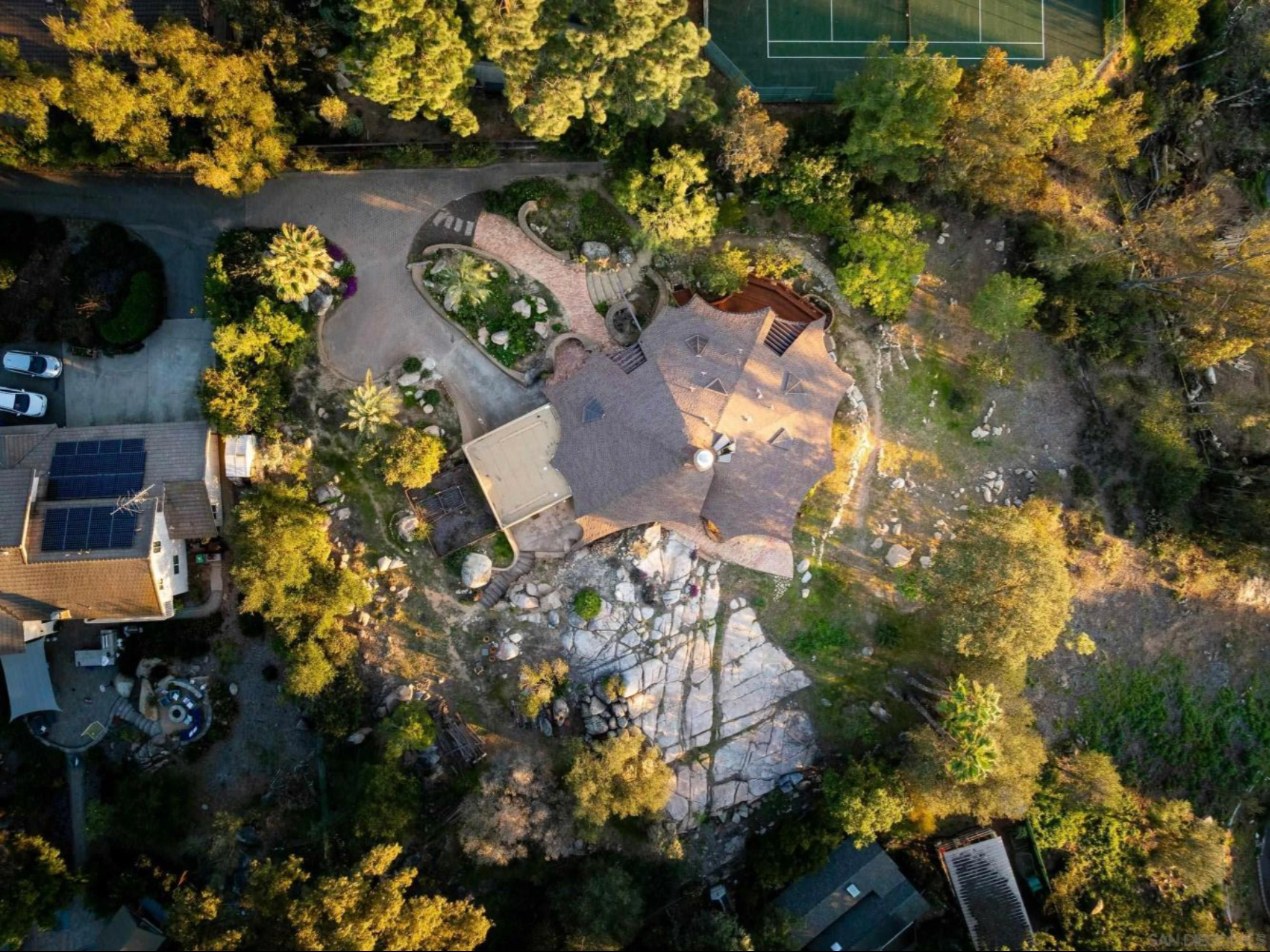 Aerial view of the Stonehill Residence at 16512 Wilderness Rd, Poway, showing its scalloped organic roof beside a granite boulder field