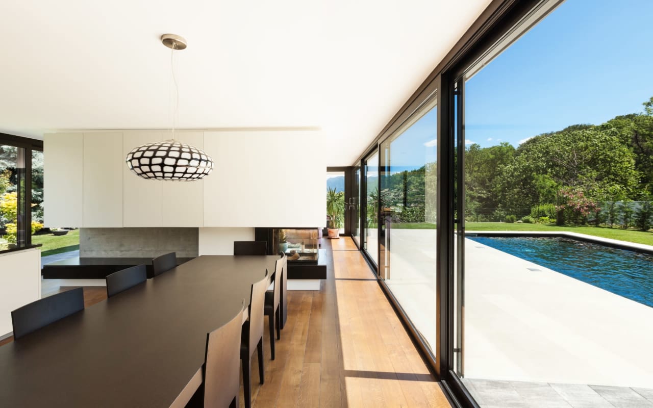 A modern dining room with a table and chairs next to a swimming pool.