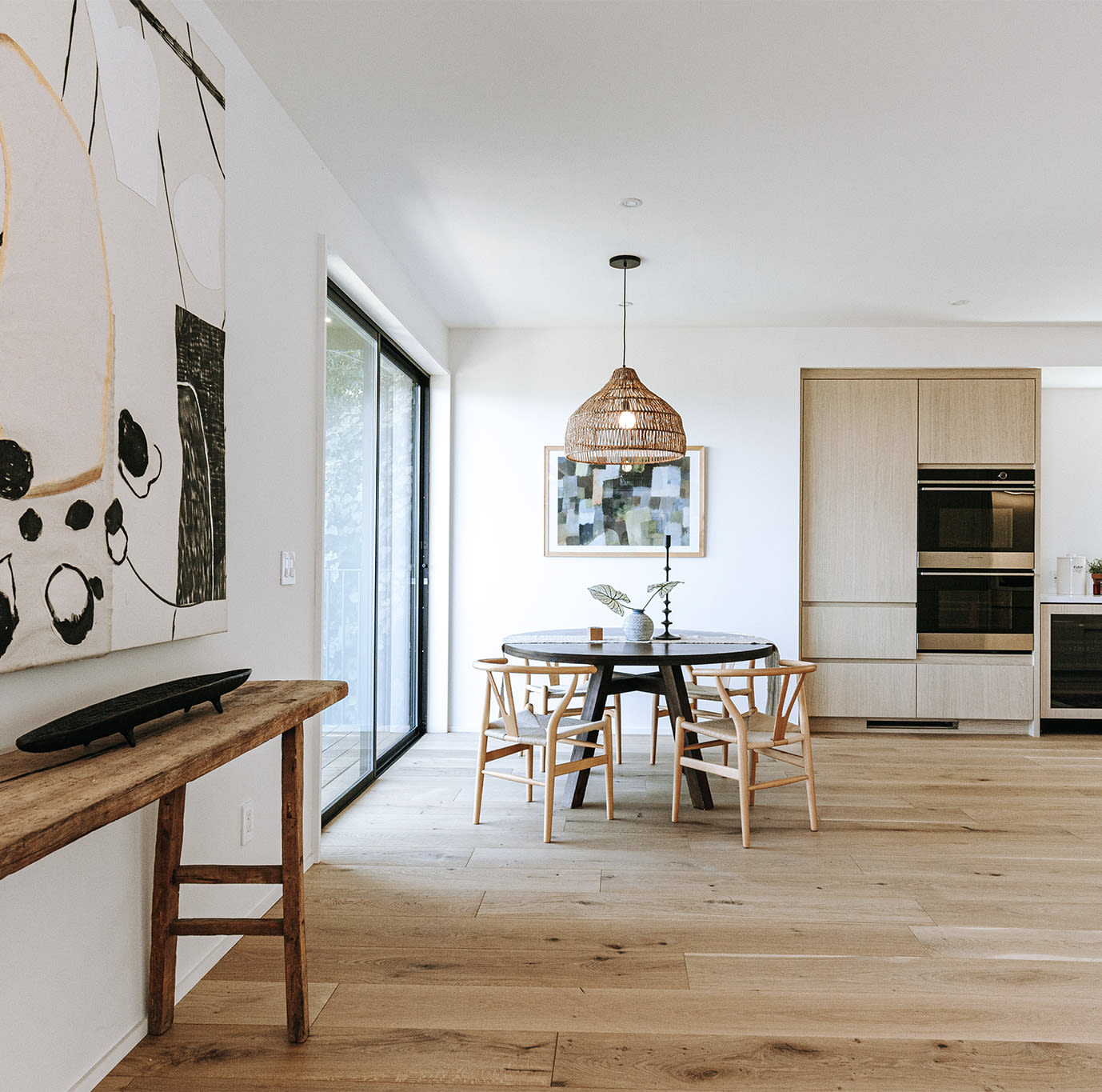 Dining area with a round table, woven pendant light, and built-in kitchen cabinetry.
