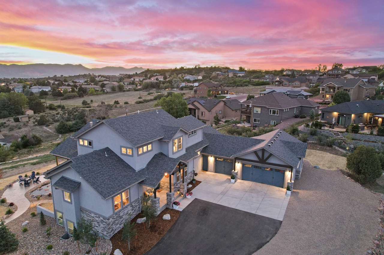Aerial view of a suburban home with a three-car garage, surrounded by landscaped yards, and neighboring houses.