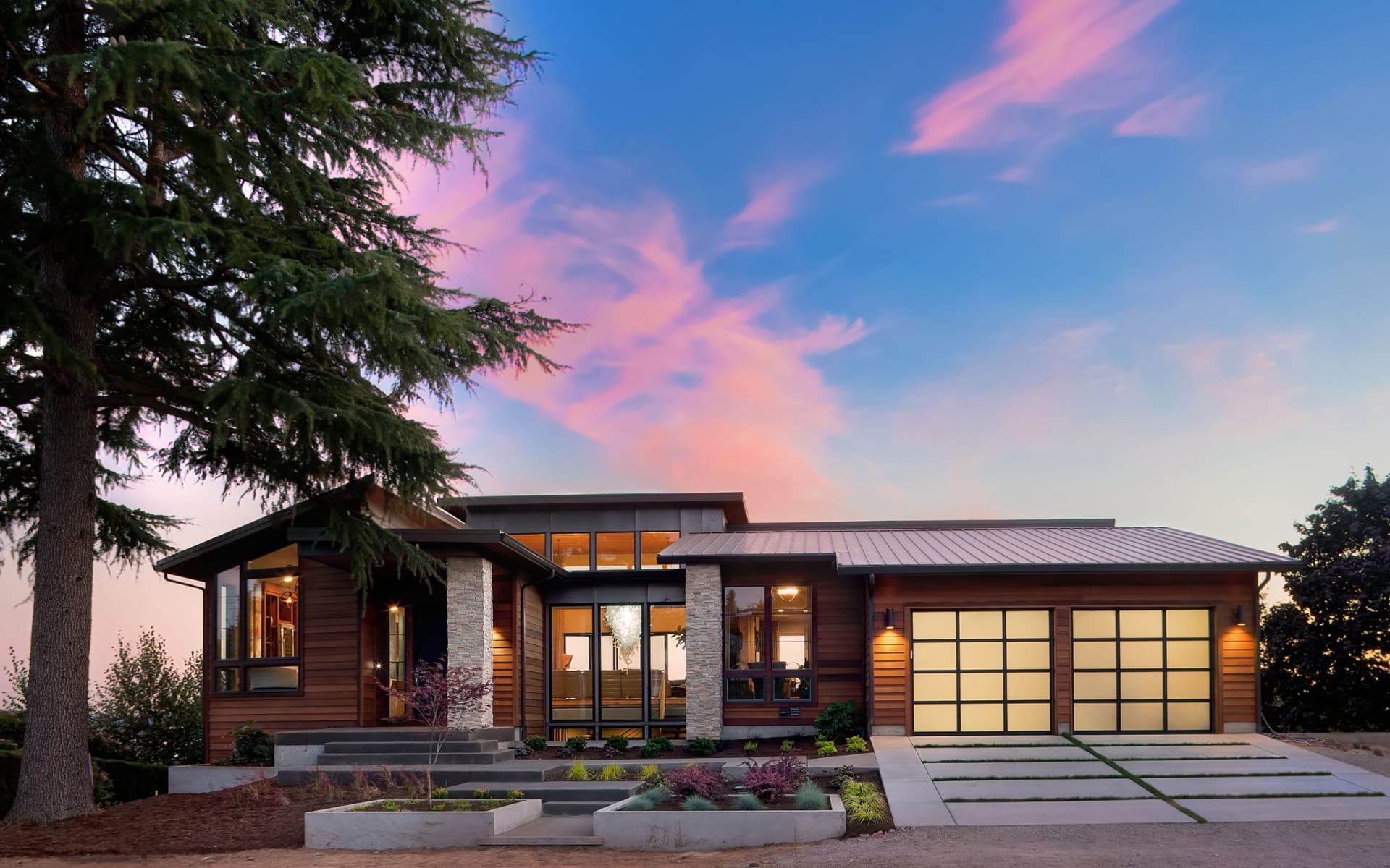  A modern single-story house with a mix of wood siding and stone accents under a dramatic sky with pink and blue hues.