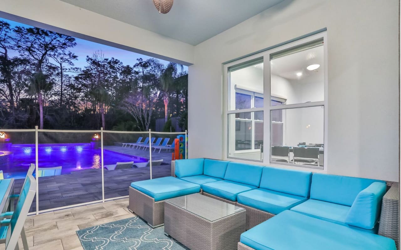 A blue outdoor couch on a stone patio next to a swimming pool. 