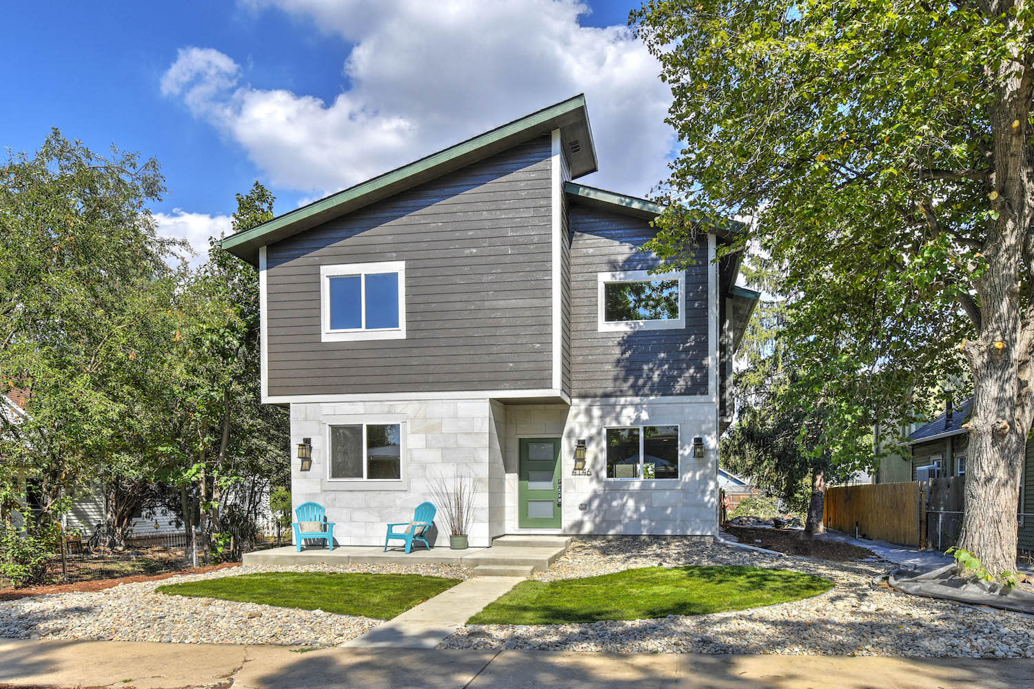  A modern two-story house with a distinct architectural design, featuring a combination of dark gray horizontal siding on the upper level and light gray stone cladding on the lower level. 