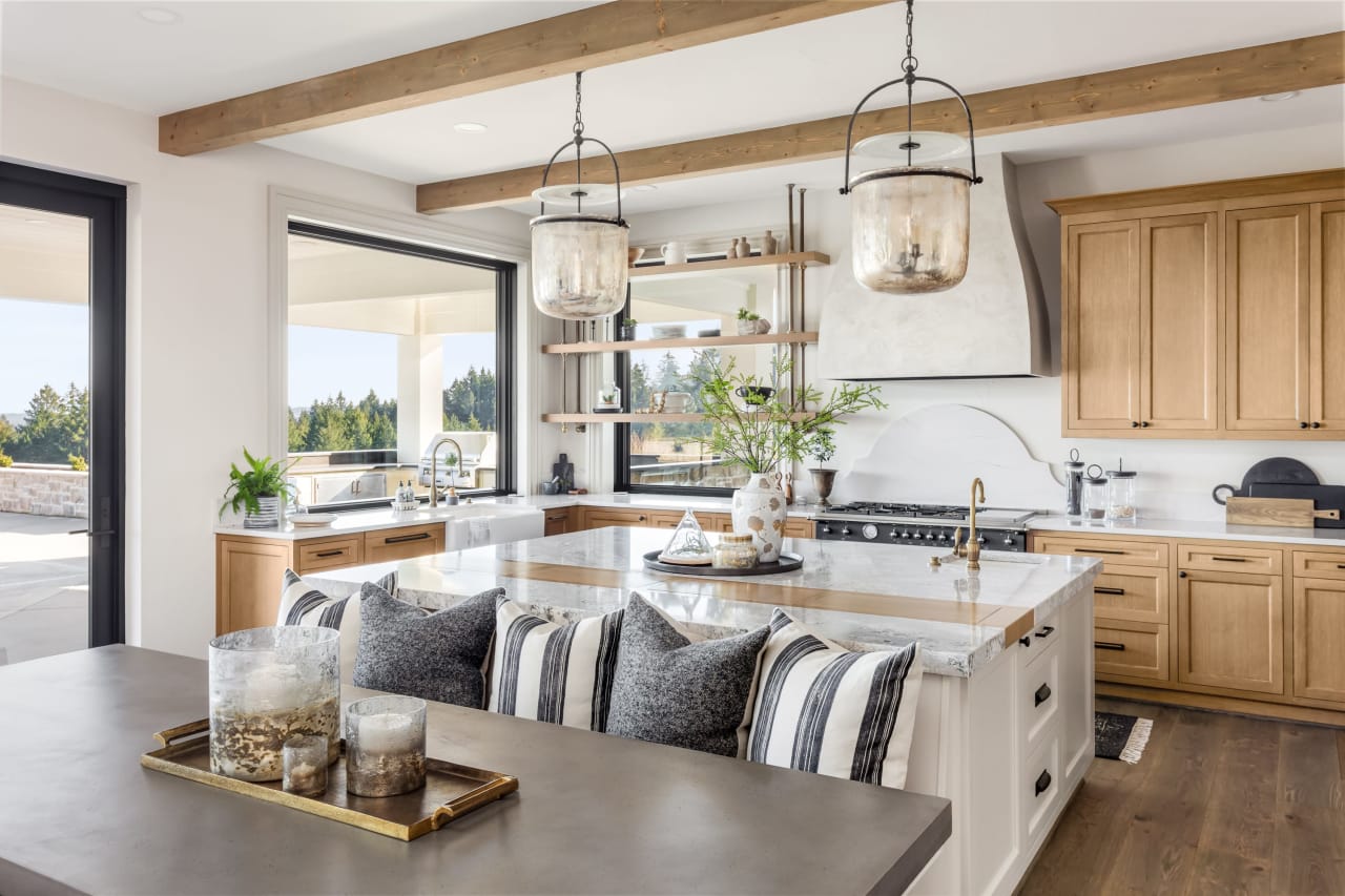 Modern kitchen with wood cabinets, marble countertops, and large windows.