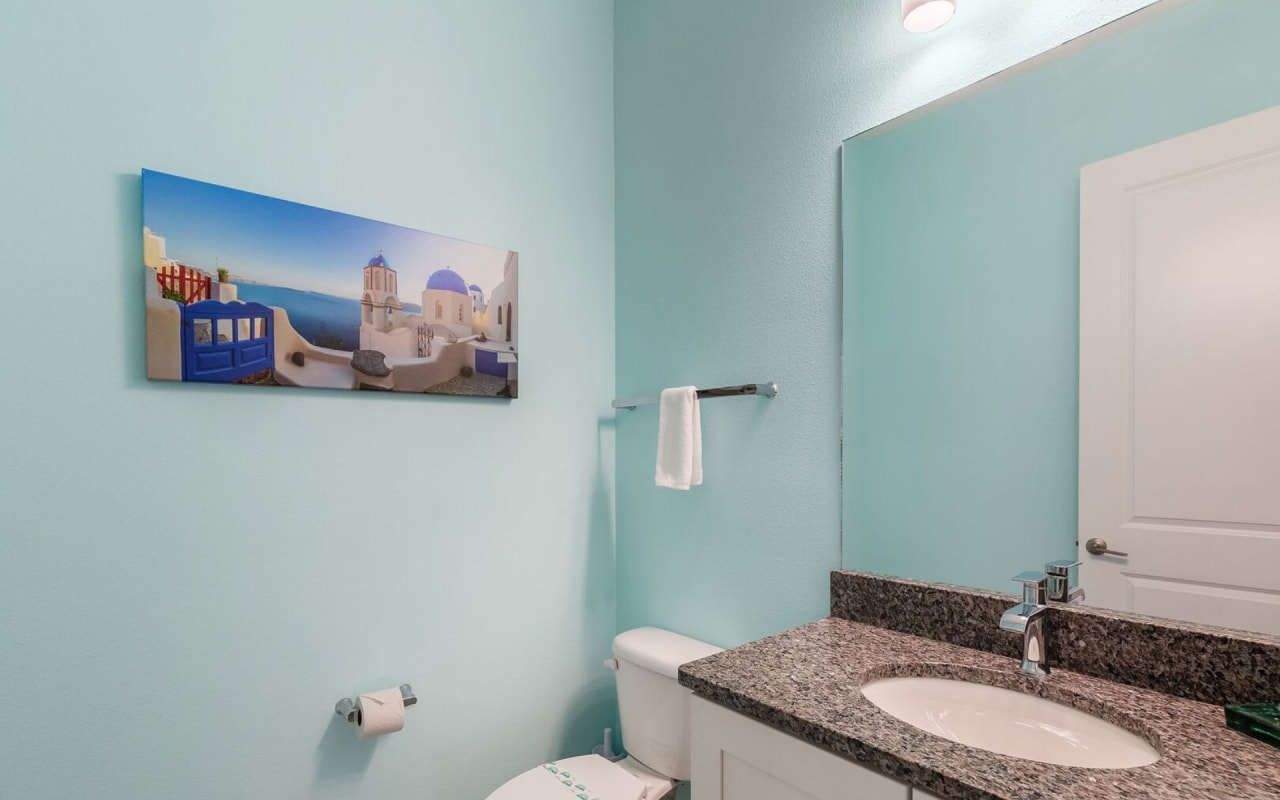 A bathroom with a toilet, sink, and a painting of Santorini on the wall.