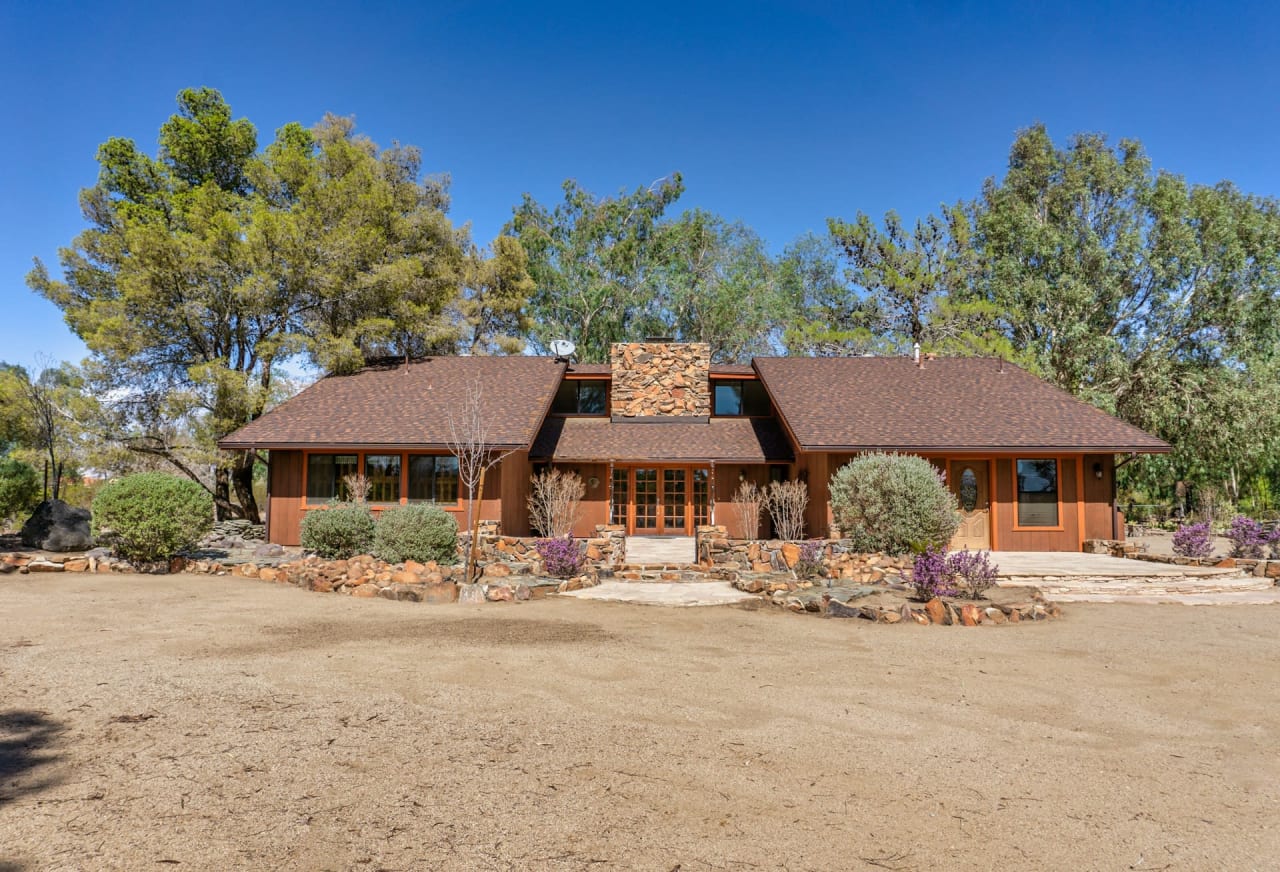 A large house with a chimney and a dirt field around it.