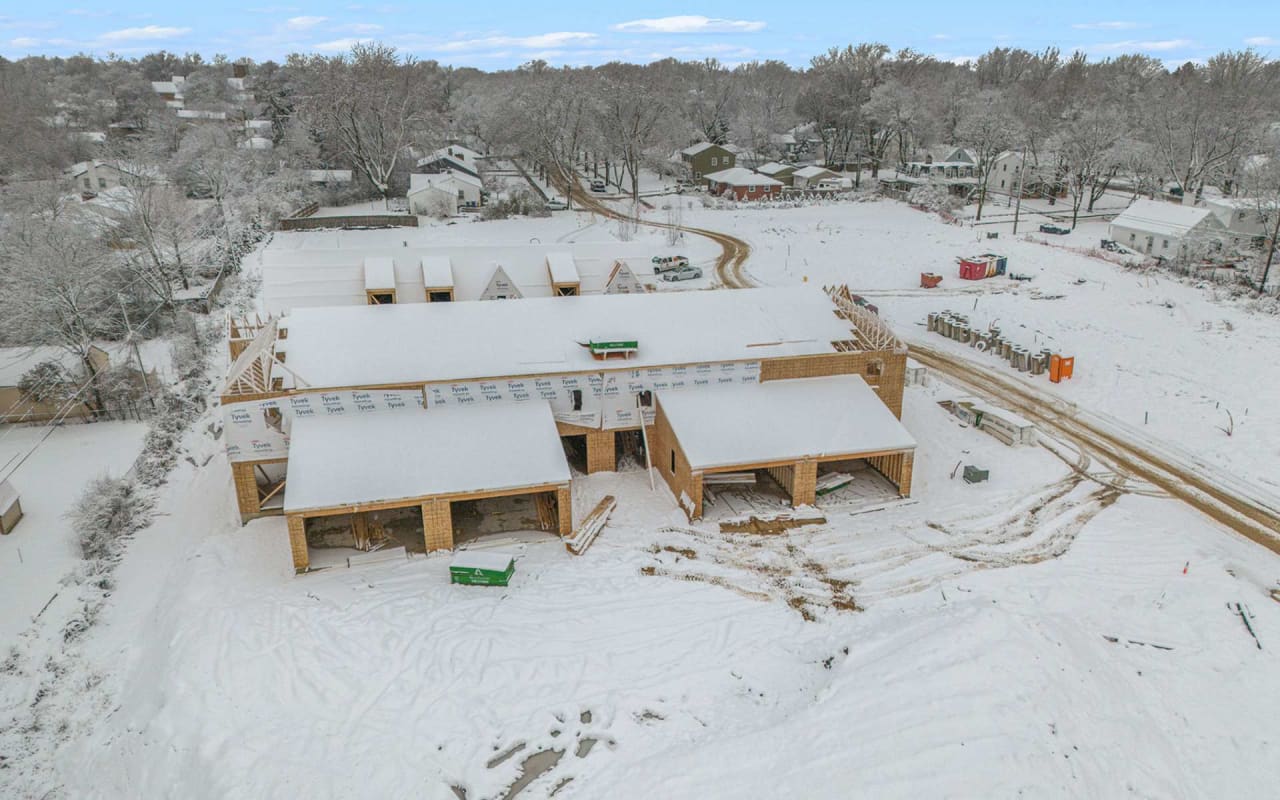 A partially built wooden house with a brown roof is under construction in a snowy field.