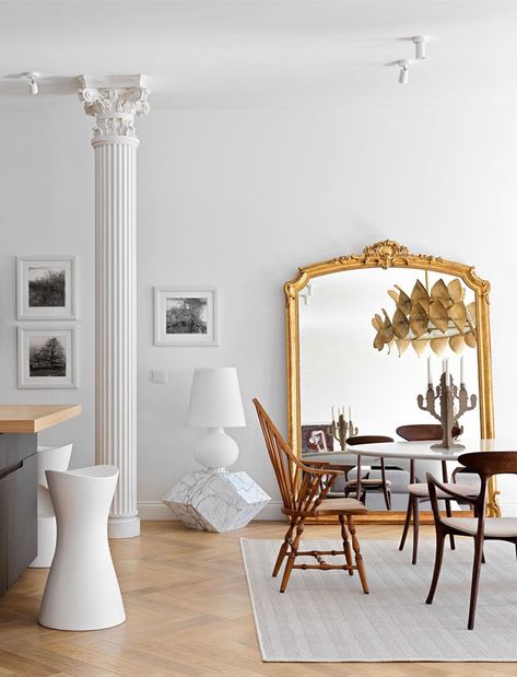 Light-filled living room with antique column, gold-framed mirror, and ornate chandelier, ideal for luxury homes or condos.