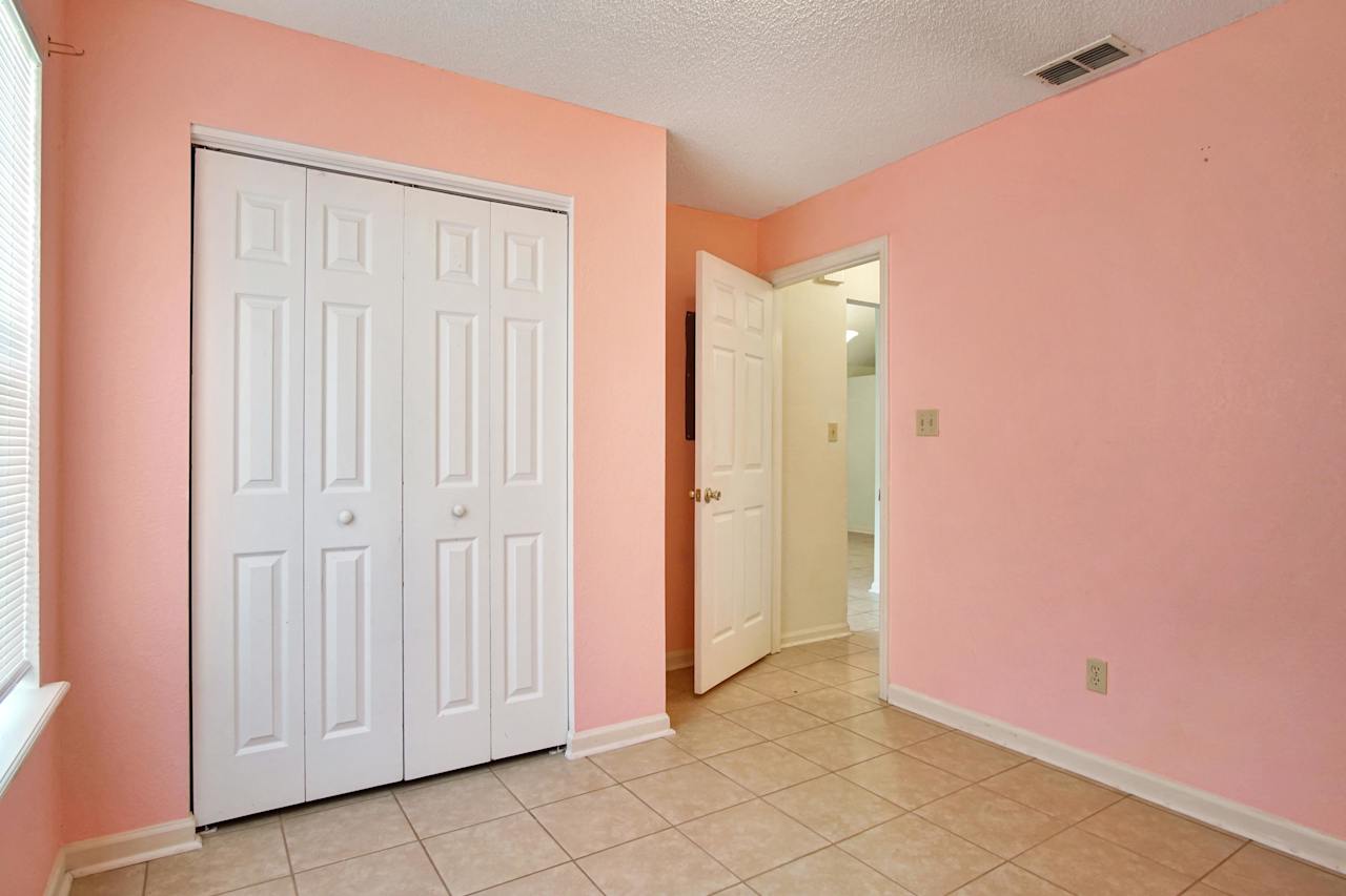 Photo of 3rd bedroom featuring double closet doors, peach wells, lightly colored tile, white ceiling, a window with white blinds, and the entrance to the main hallway  at 2709 Oak Park Court, Tallahassee, Florida 32308