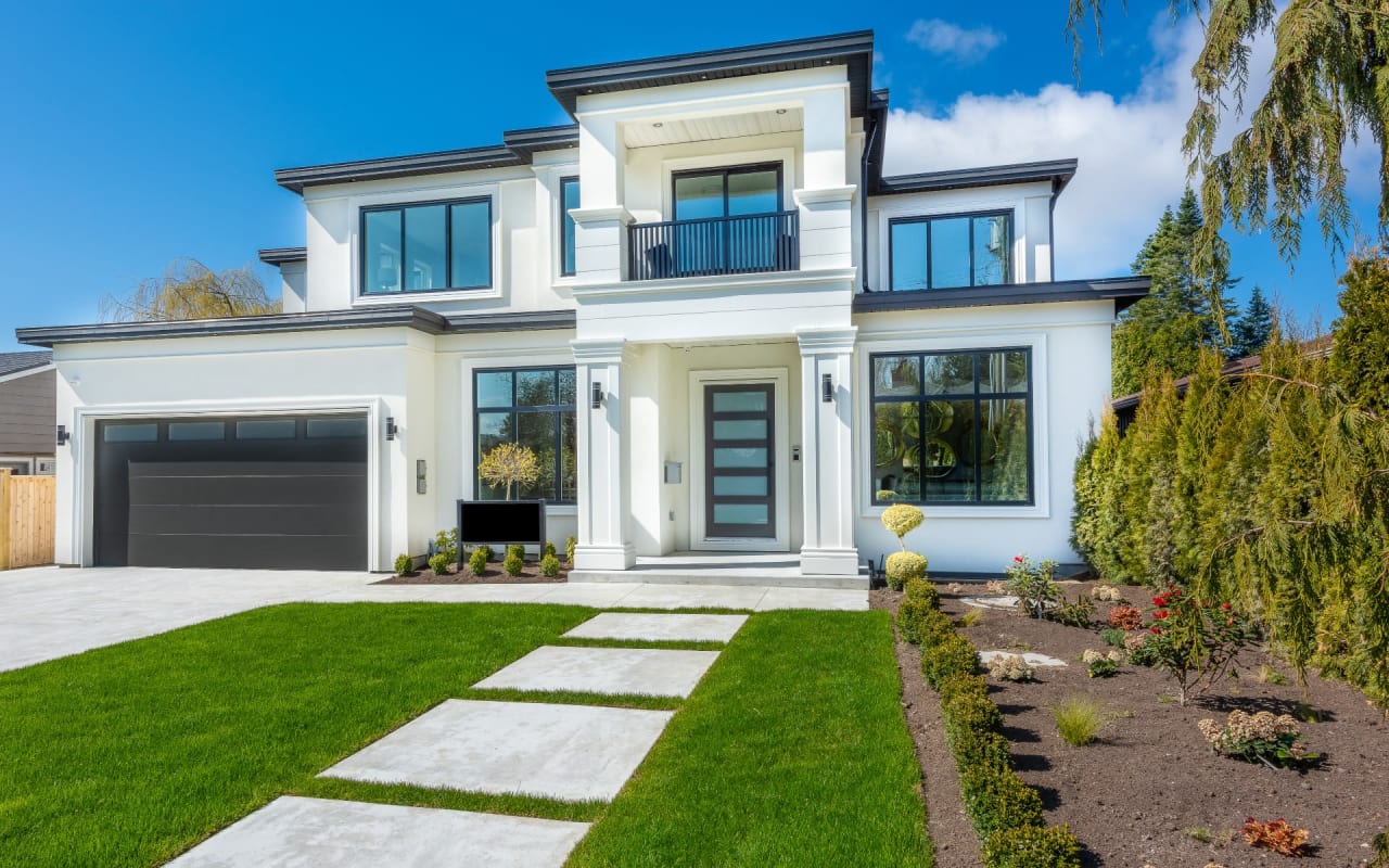 A two-story white house with a black garage, gabled roof, porch, large black-framed windows, and brick walkway.