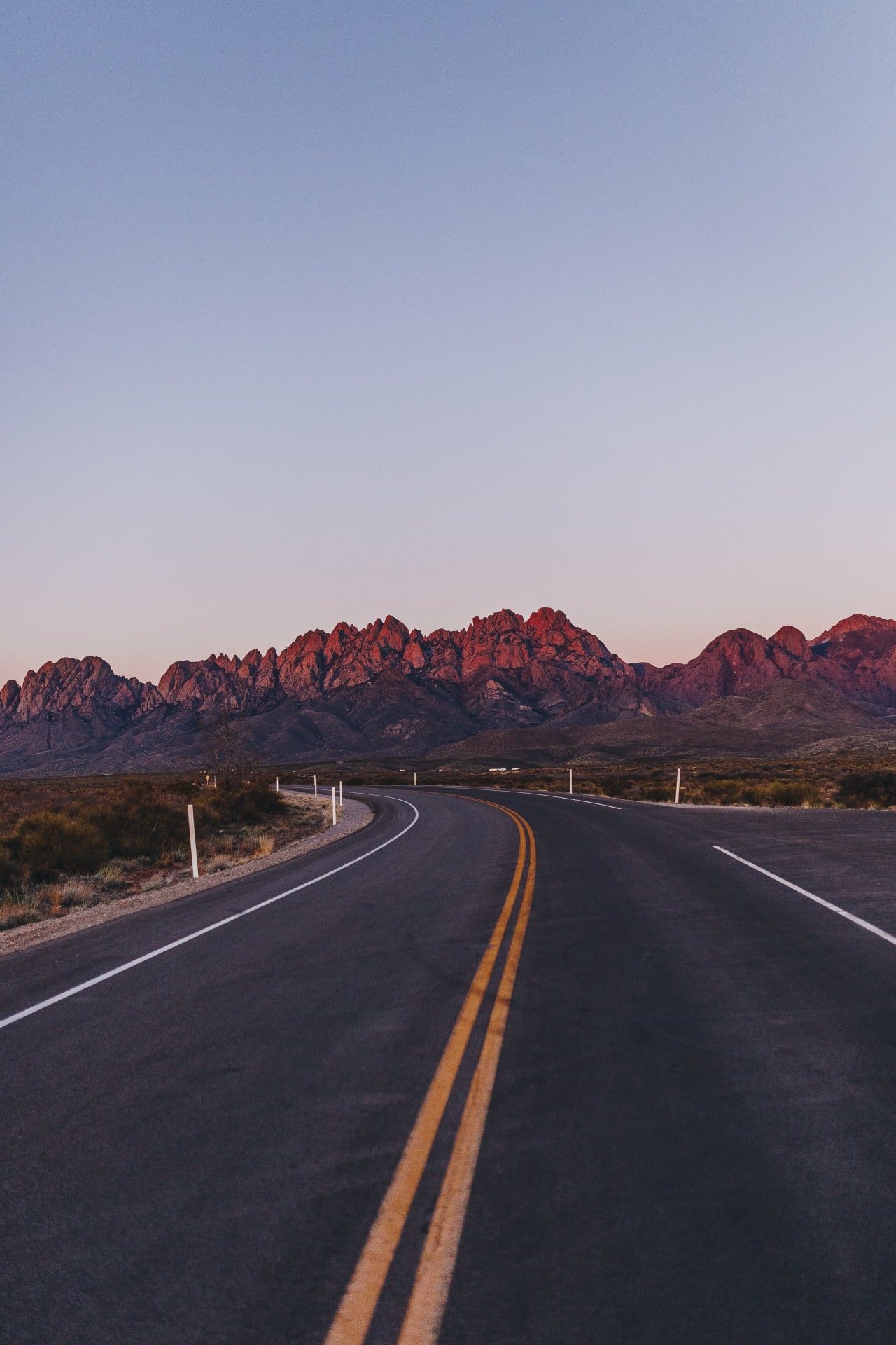 An empty asphalt road leading towards mountains in the distance.