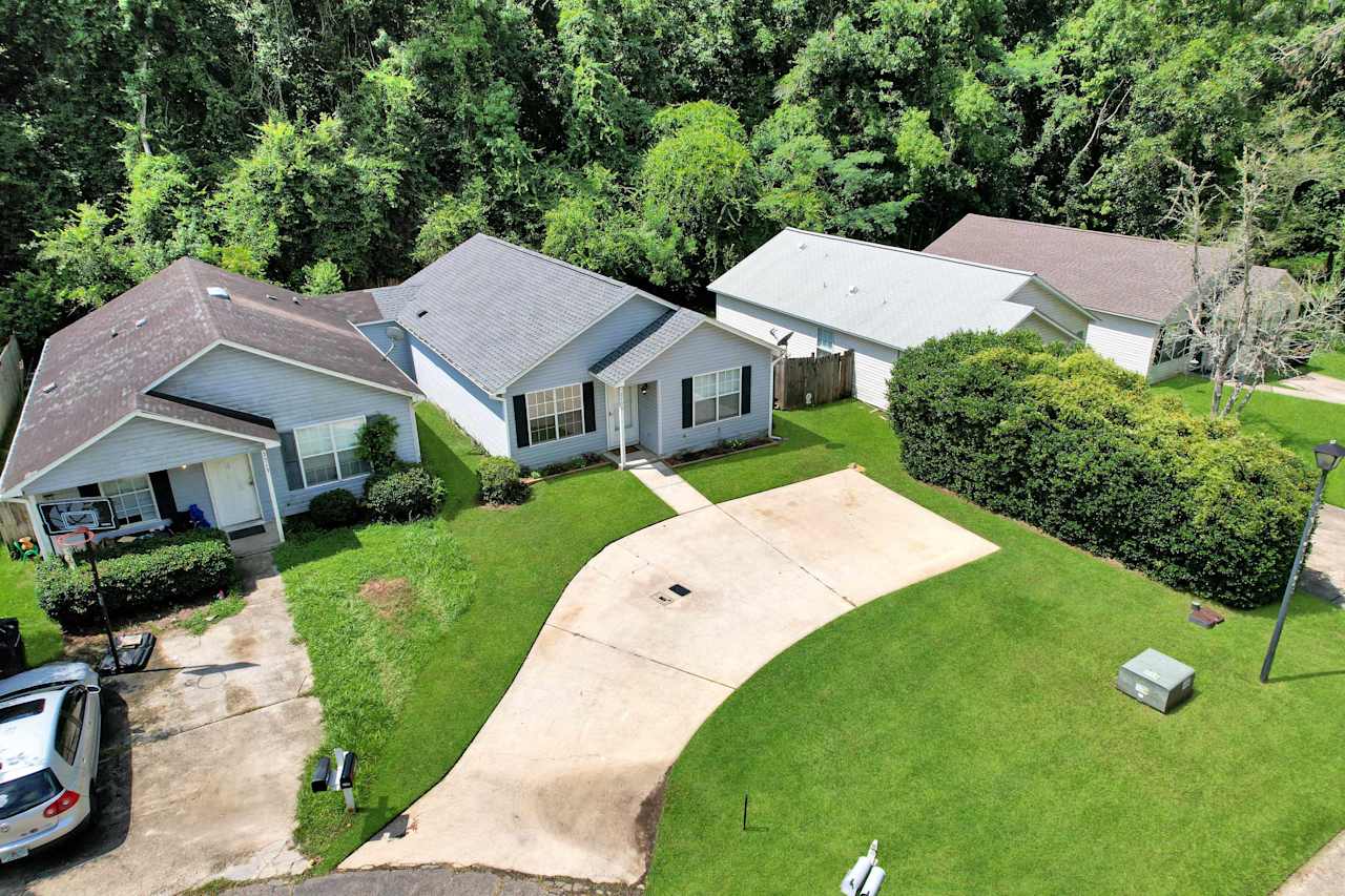 Drone or aerial photo of home featuring a semicircle driveway, a paved walkway to the front door, green grass, a fence yard, And garden beds  at 2709 Oak Park Court, Tallahassee, Florida 32308