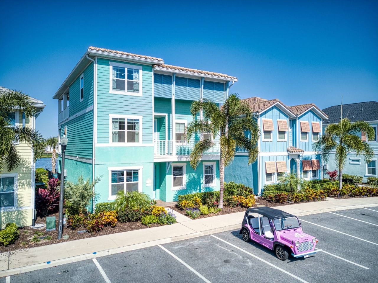 A pink golf cart parked in front of a colorful building with a blue roof and white facade.