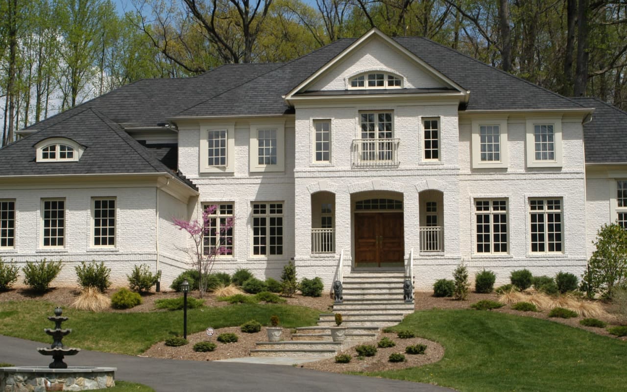 A grand two-story white house with six-over-six shutters, a stone pathway to the front door, and a front fountain and lawn.