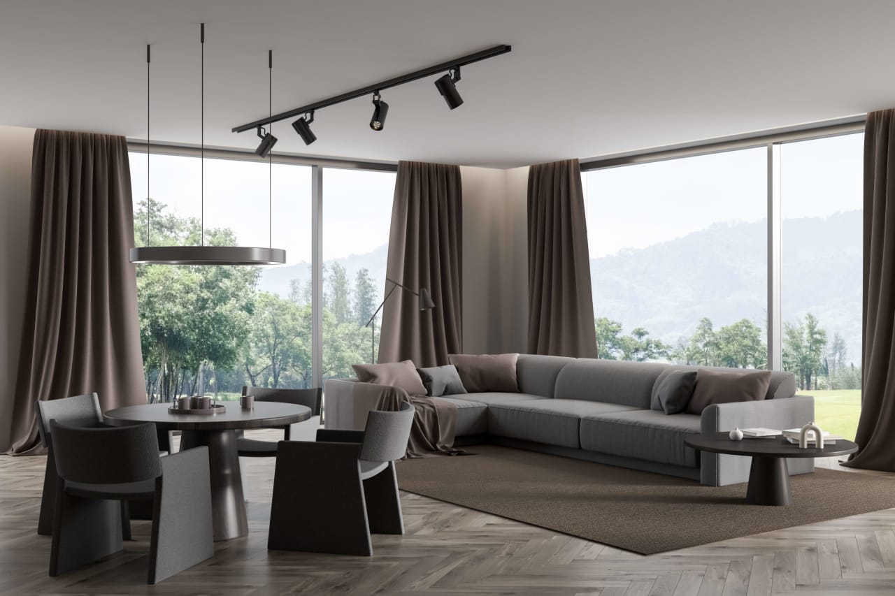 A spacious living room with a large black couch and sheer curtains lining the tall windows.