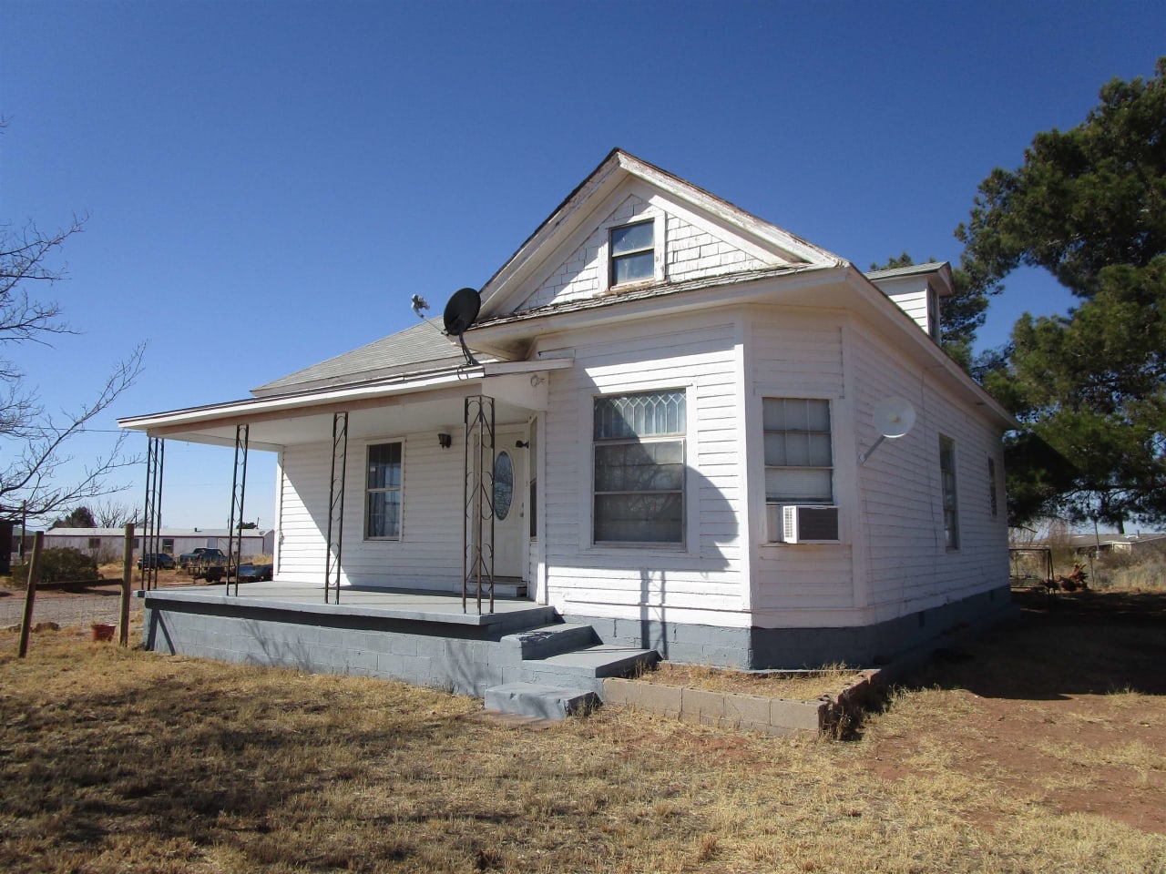 A white house with a satellite dish on the roof and a porch in the middle of a field.