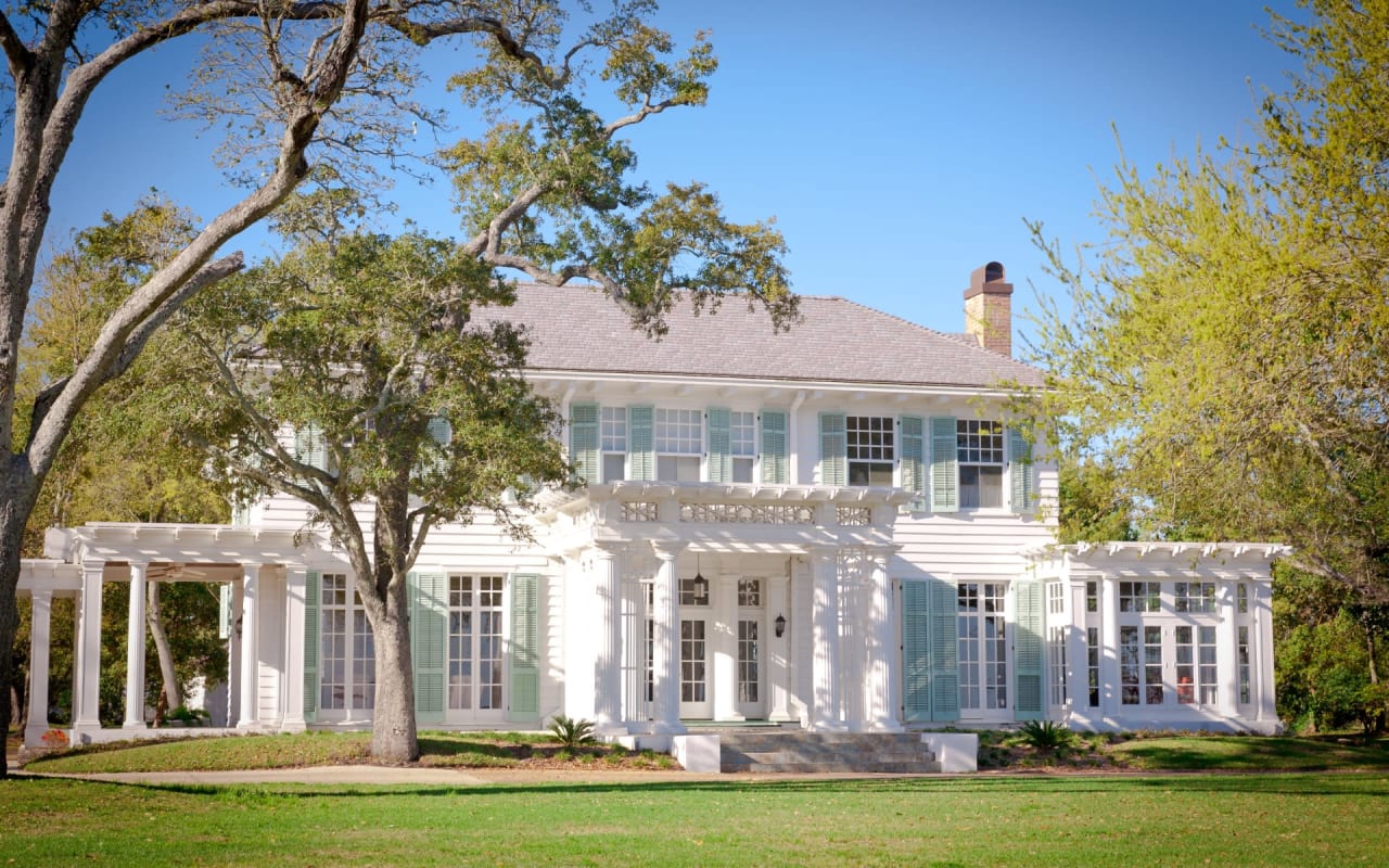 A large white house with white shutters in a field.