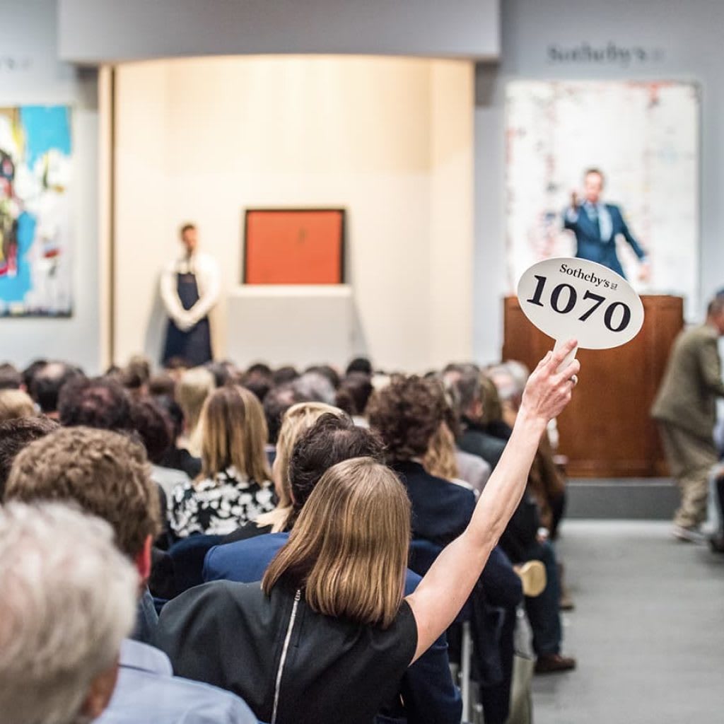 Auction attendee raises a Sotheby's 1070 bidding paddle at a crowded indoor auction.