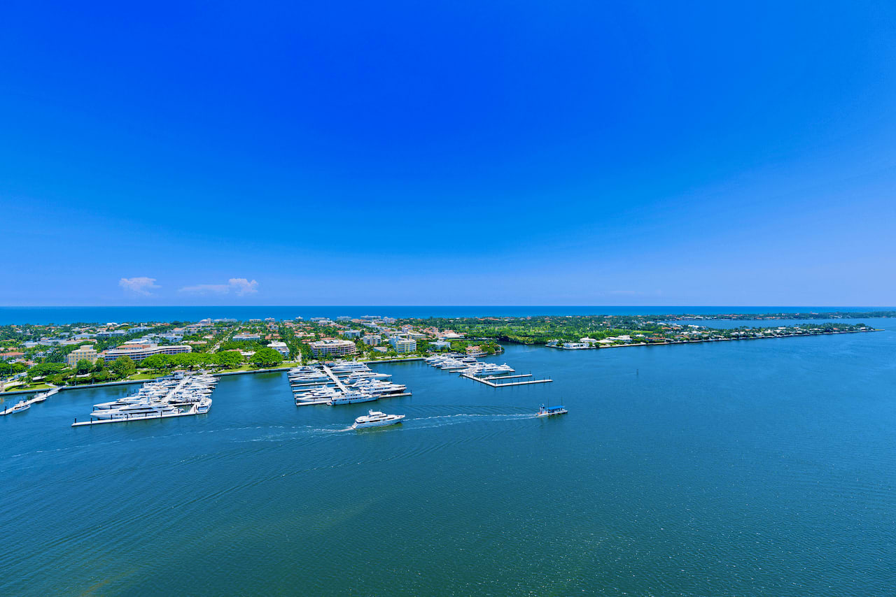  Aerial view of Palm Beach marina with numerous boats docked, set against a coastal cityscape with buildings and greenery, under a clear blue sky and view of Atlantic Ocean