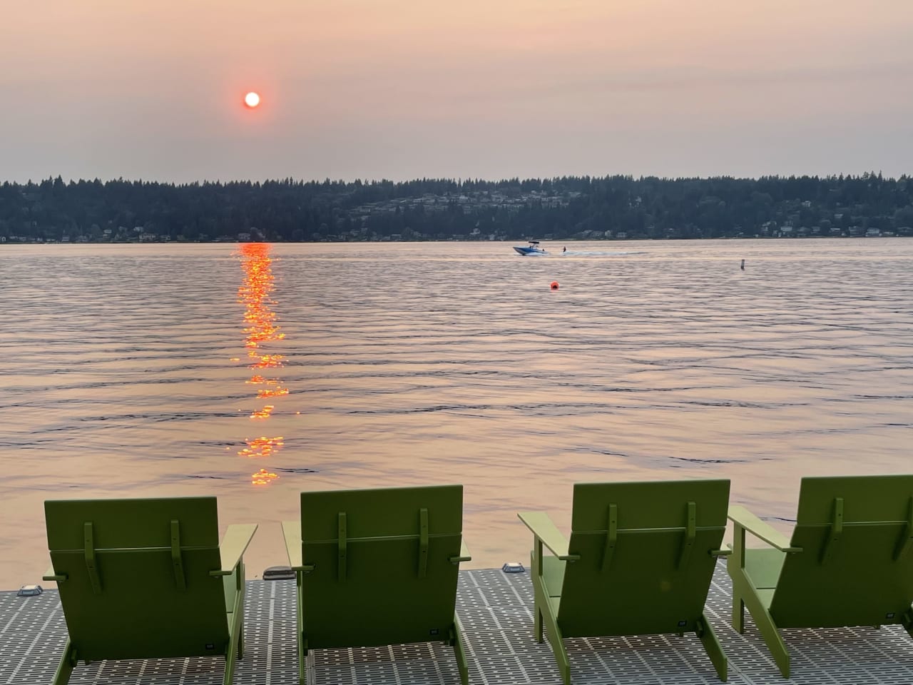 A row of green chairs sitting on a dock next to a lake with a boat in the distance