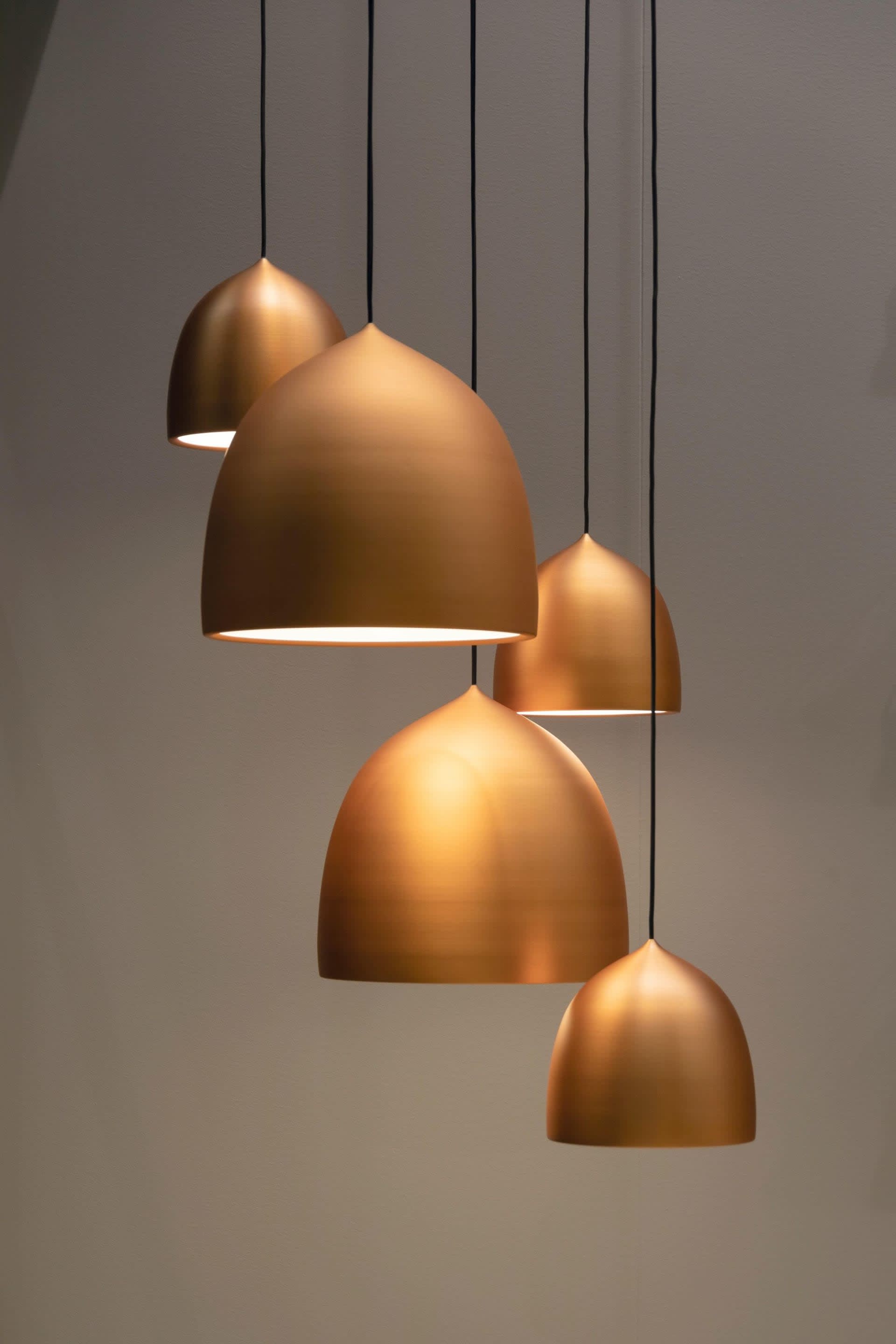 Five staggered copper pendant lights with rounded shades hang against a gray wall.
