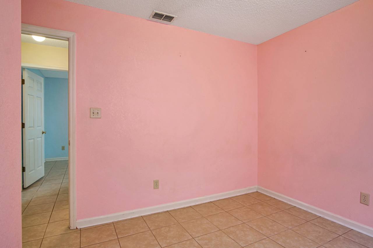 photo of third bedroom featuring peach walls, white ceiling, lightly colored tiled floors, white baseboards, and a view of the main hallway at 2709 Oak Park Court, Tallahassee, Florida 32308