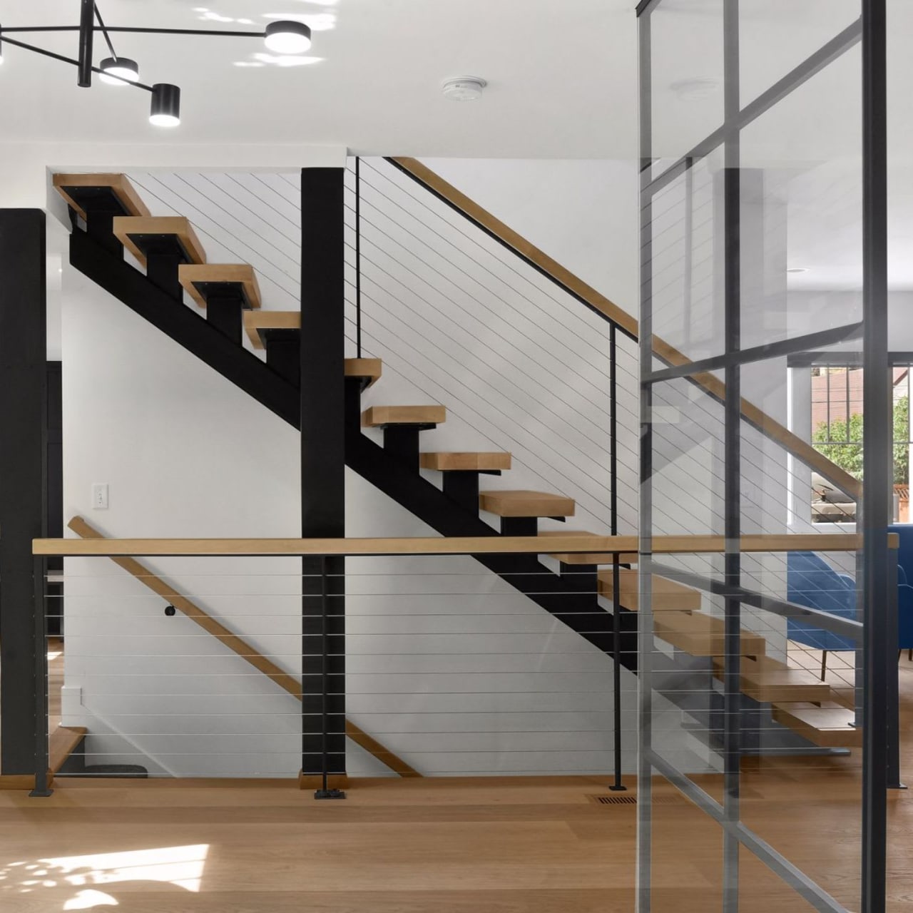 A modern staircase with light-colored wooden steps and a thin black metal railing.