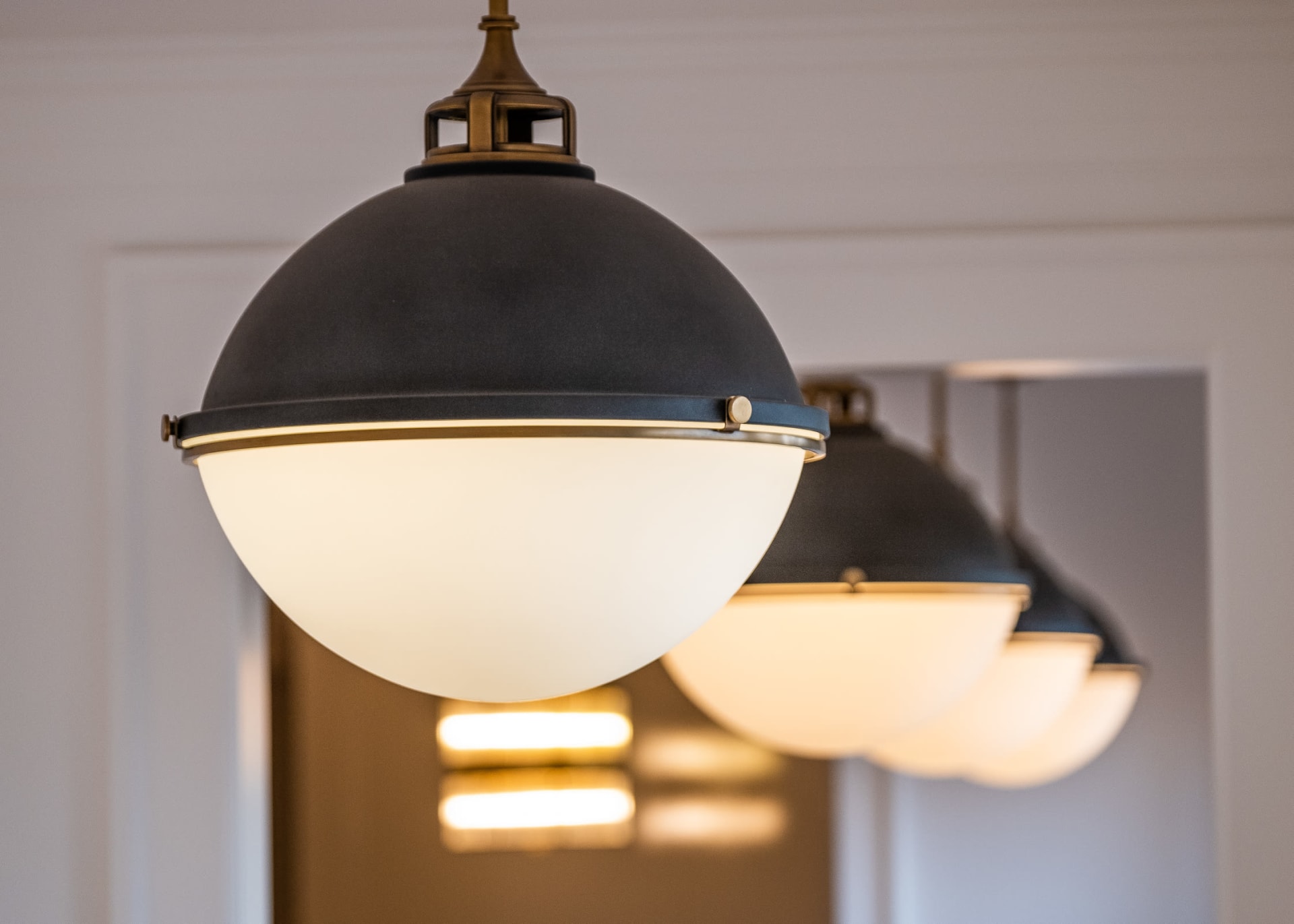 A close-up shot of three modern globe pendant lights, featuring dark gray domes with brass accents and frosted white glass globes, hanging in a row. 
