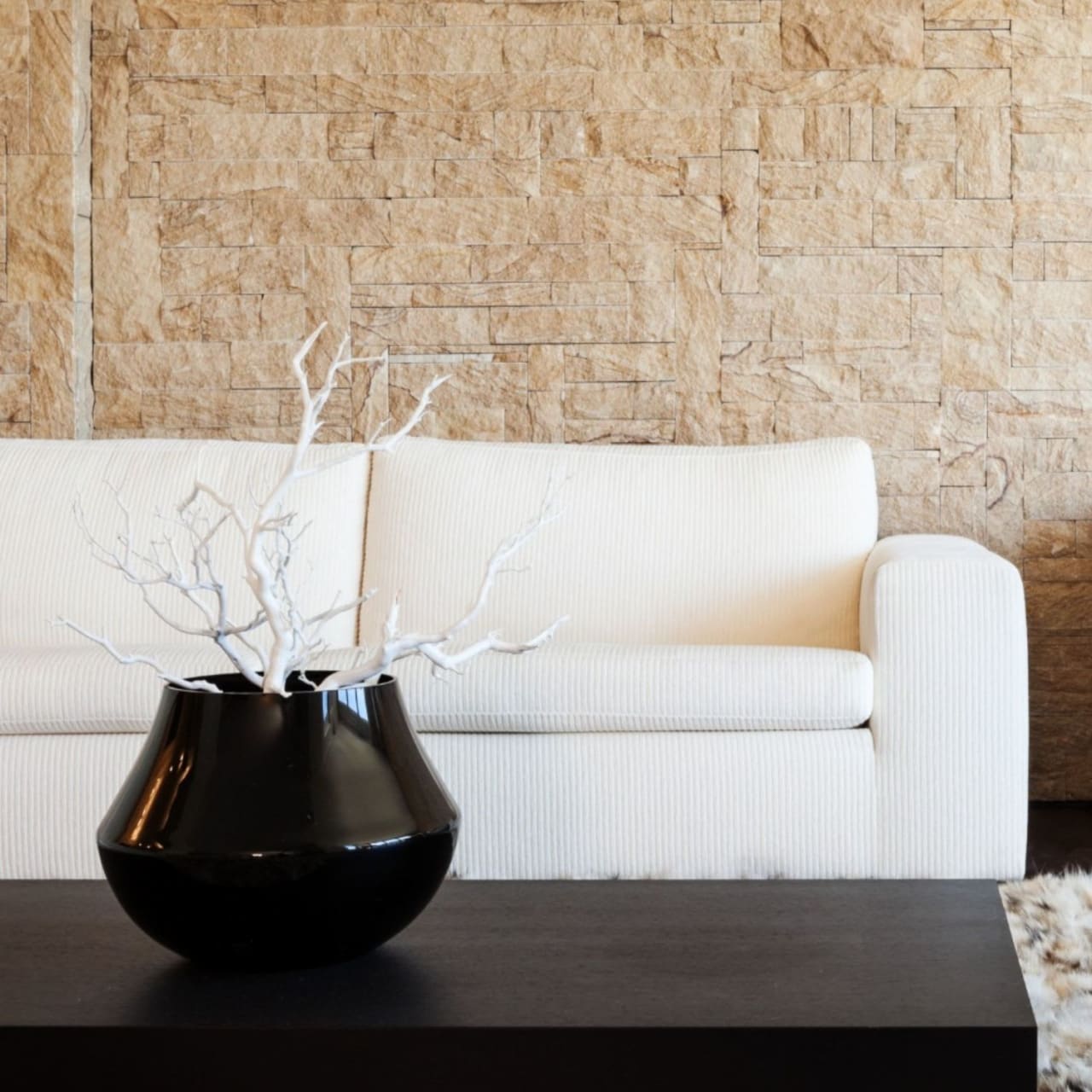 A black vase sits on a rectangular wooden coffee table in front of a white couch.