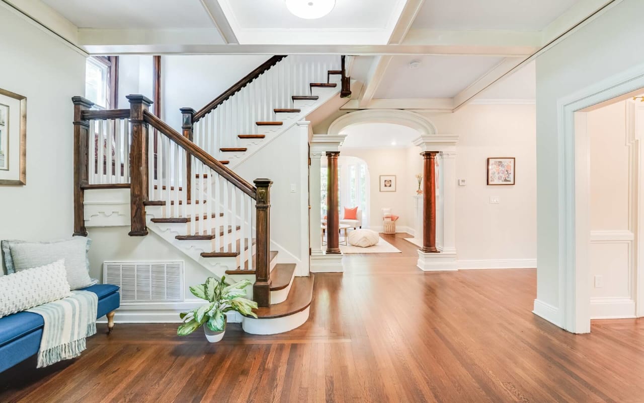 Elegant foyer with a wooden staircase, arched entryways, and hardwood floors, leading to a bright living room area.