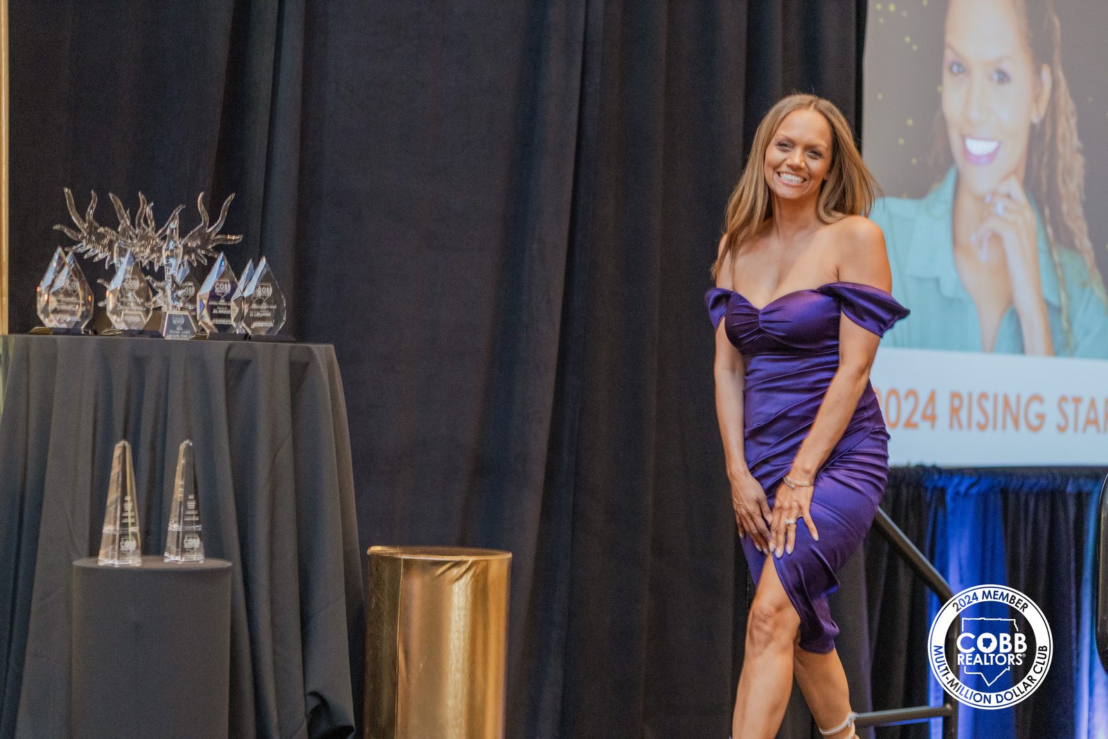 Lawana Ludd smiling on stage as the 2024 Rising Star screen is displayed at the Cobb Association of Realtors awards gala