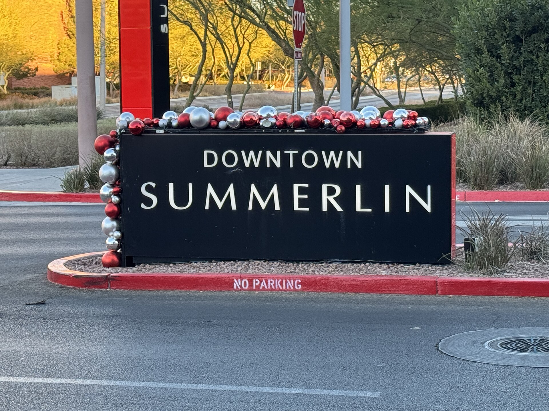 Black Downtown Summerlin entrance sign decorated with red and silver holiday ornaments in a landscaped median