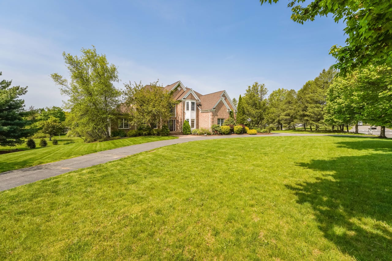 Brick house with large windows, surrounded by a well-maintained lawn and mature trees, with a long driveway.