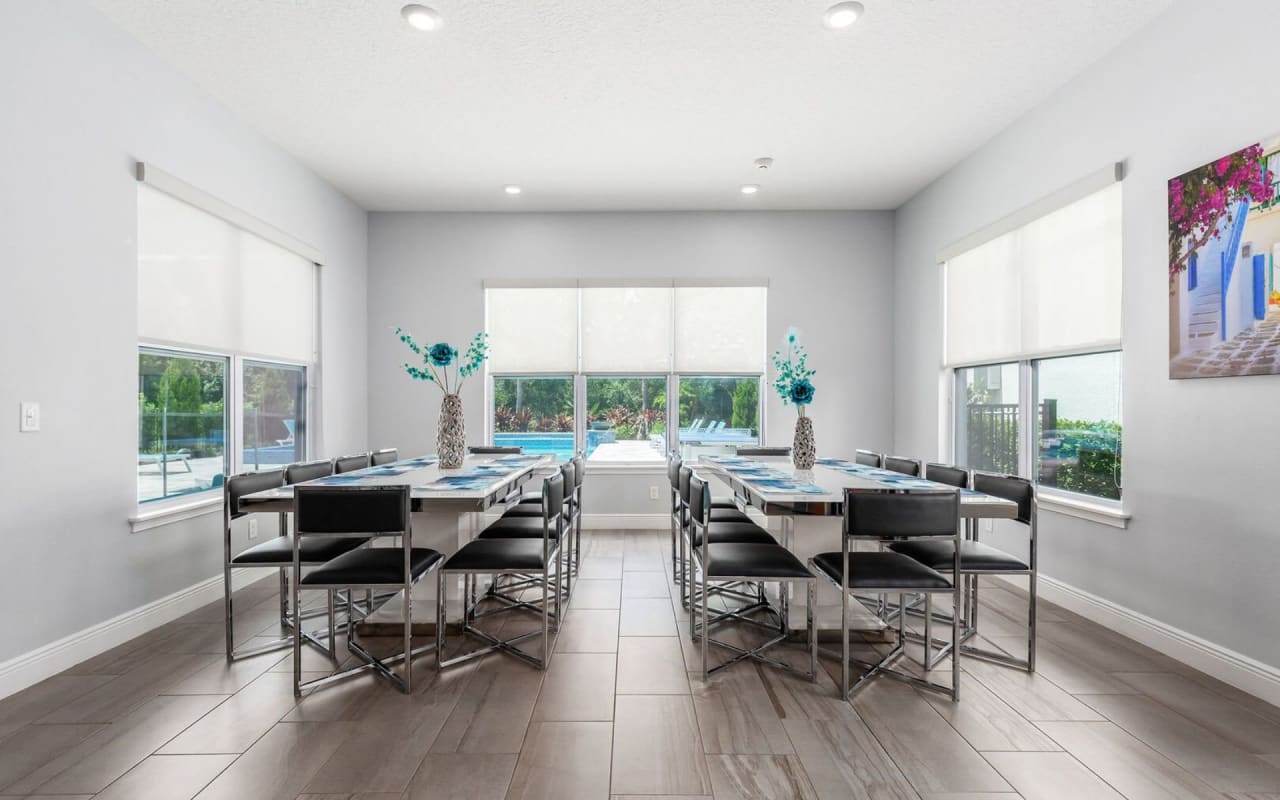 A dining room with a long wooden table with a white top and black leather chairs.