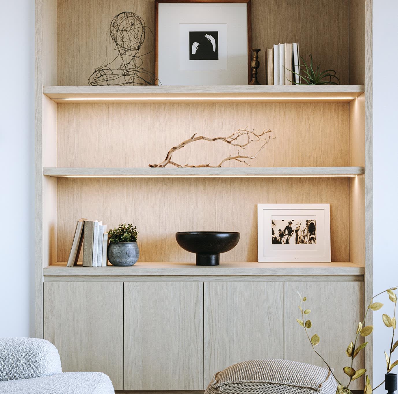 Built-in living room shelves with warm lighting, framed art, books, and sculptural decor.