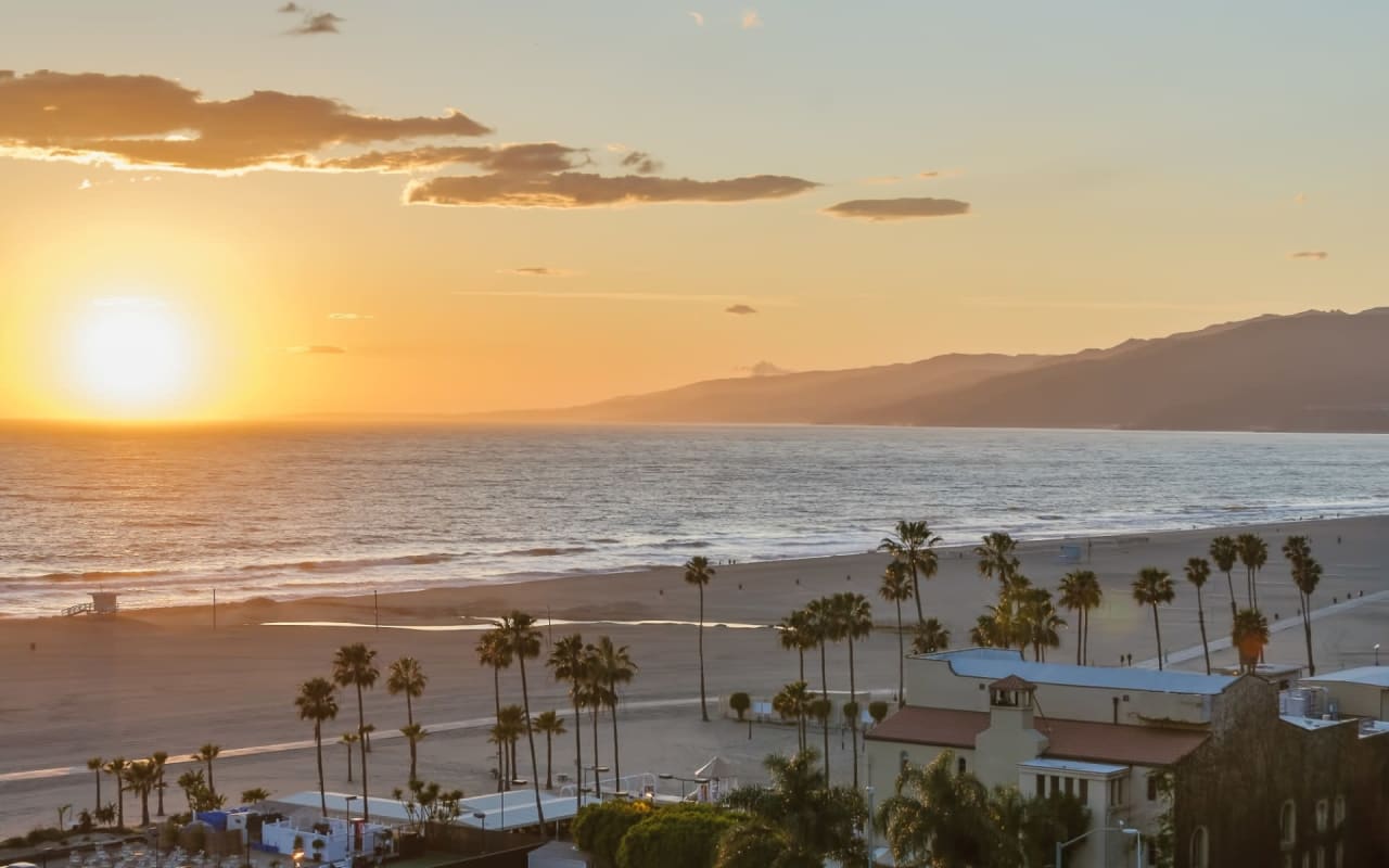 Sunset over a beach with palm trees and mountains in the background