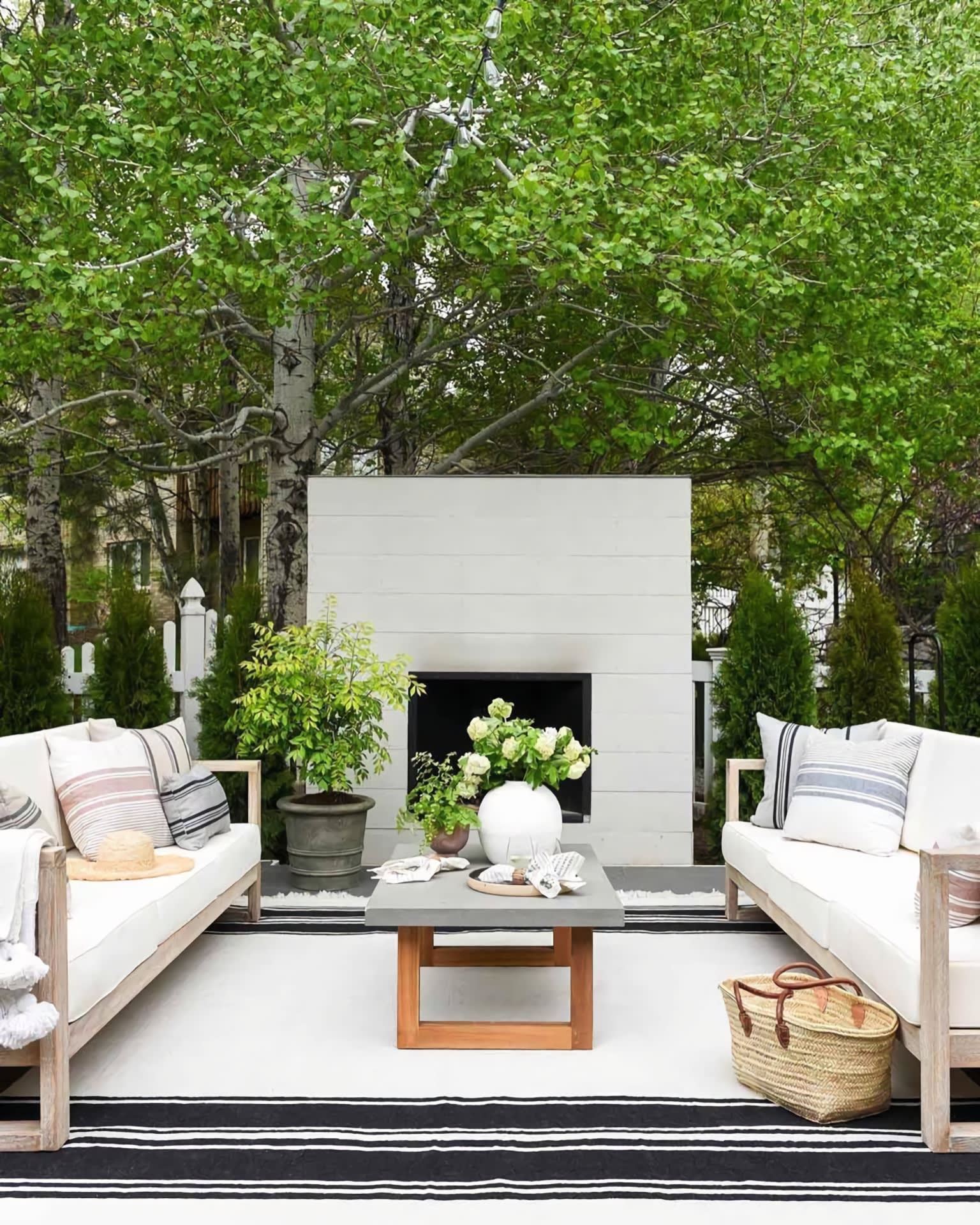 Outdoor patio with white sofas, a modern fireplace, and leafy trees
