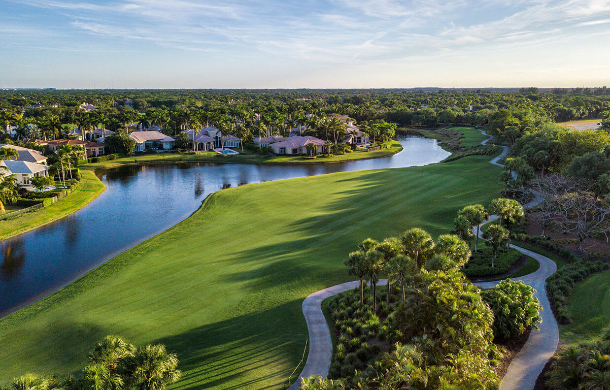 Aerial view of a golf course and winding waterway bordered by palm-lined homes.