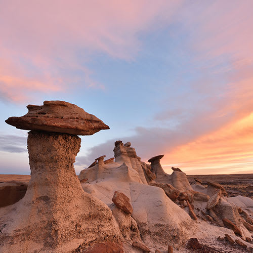 A group of unusual rock formations in a desert landscape at sunset.