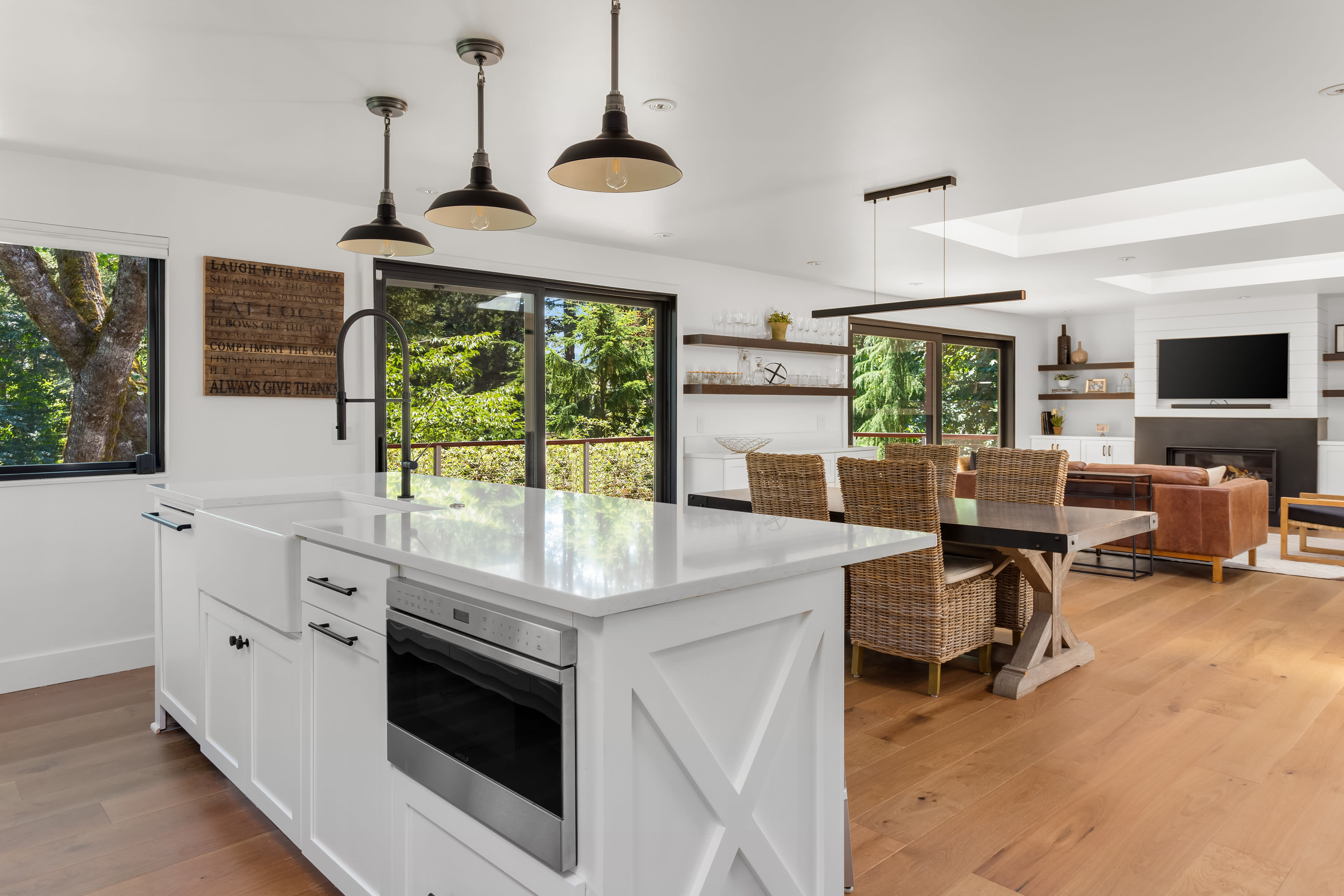 Kitchen with a large white island, pendant lights, and windows overlooking leafy trees.