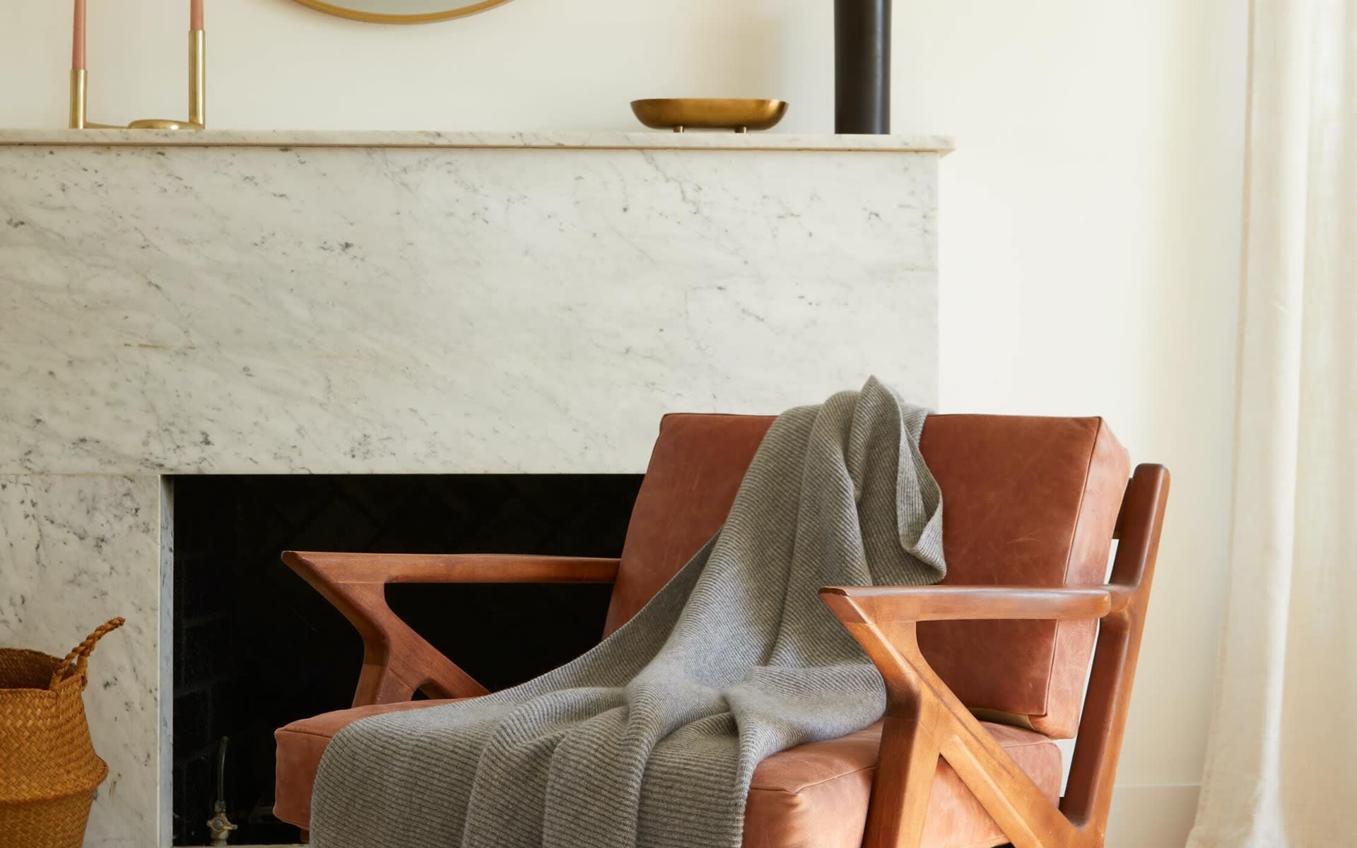Living room with a marble fireplace and cognac leather armchair draped with a gray throw.